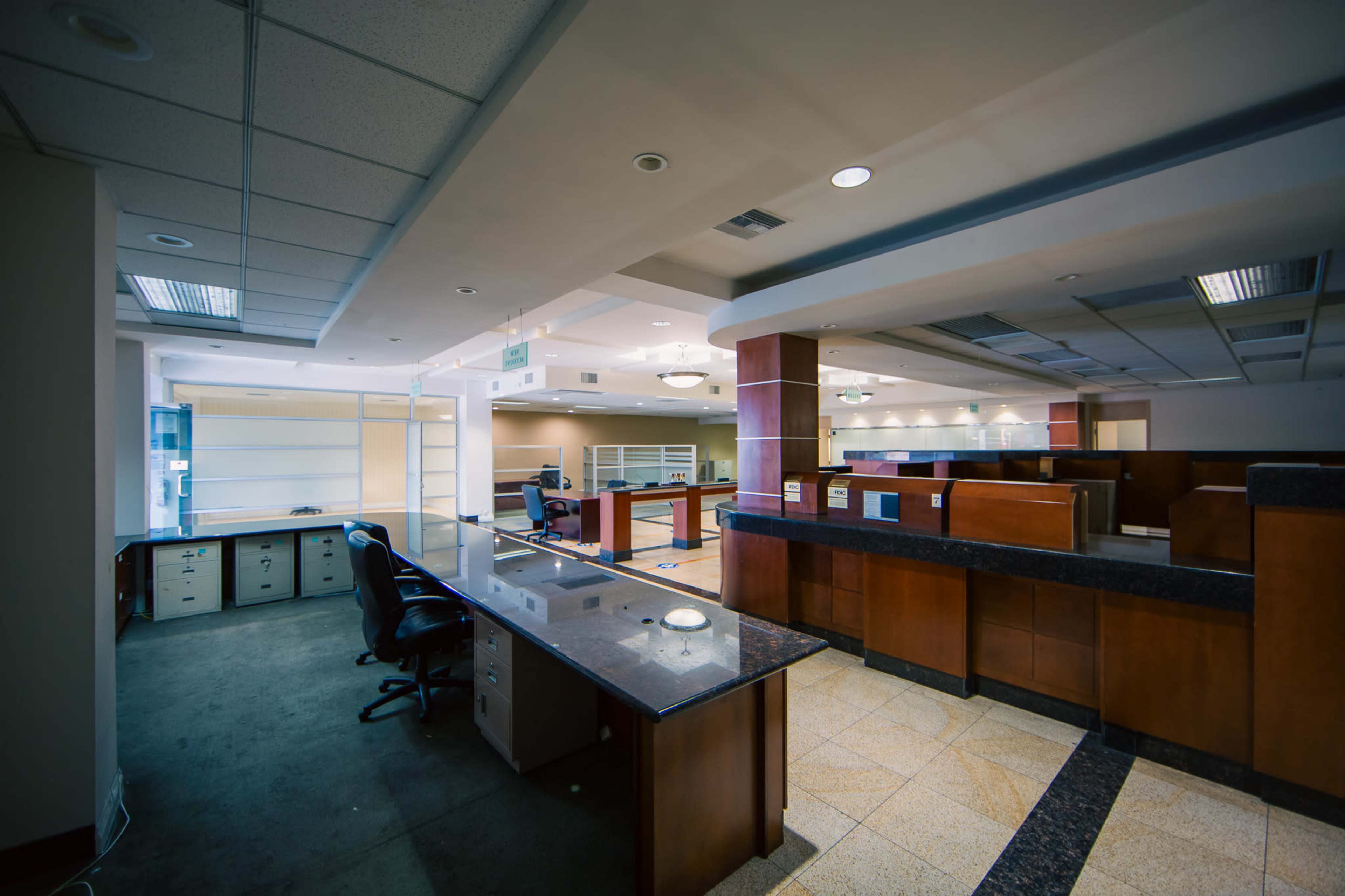 The image shows a modern office interior with desk workstations, glass partitions, and polished tile flooring.