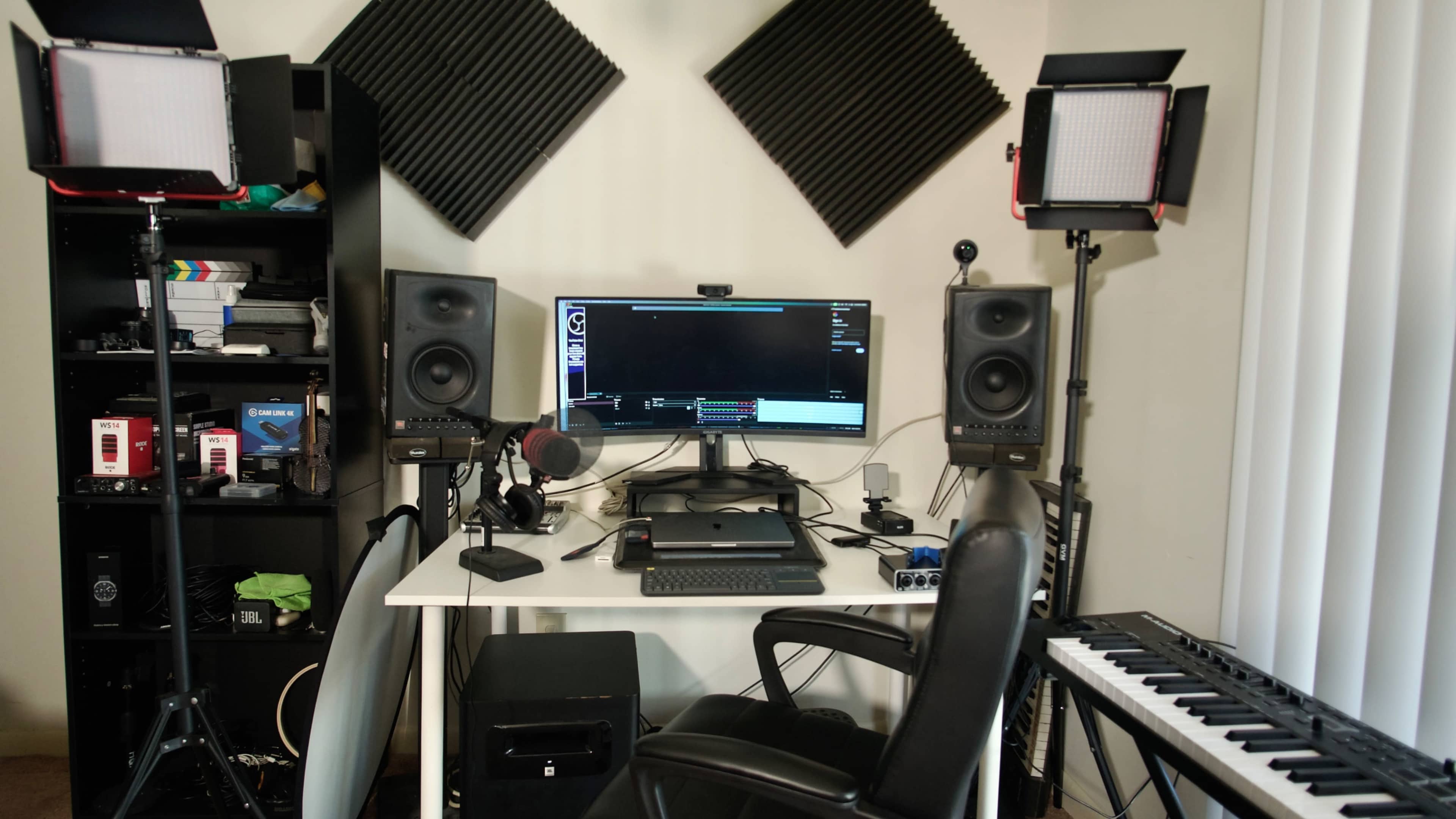 The image shows a home recording studio setup with a desk, computer monitor, audio speakers, a microphone, and various music equipment including a keyboard.