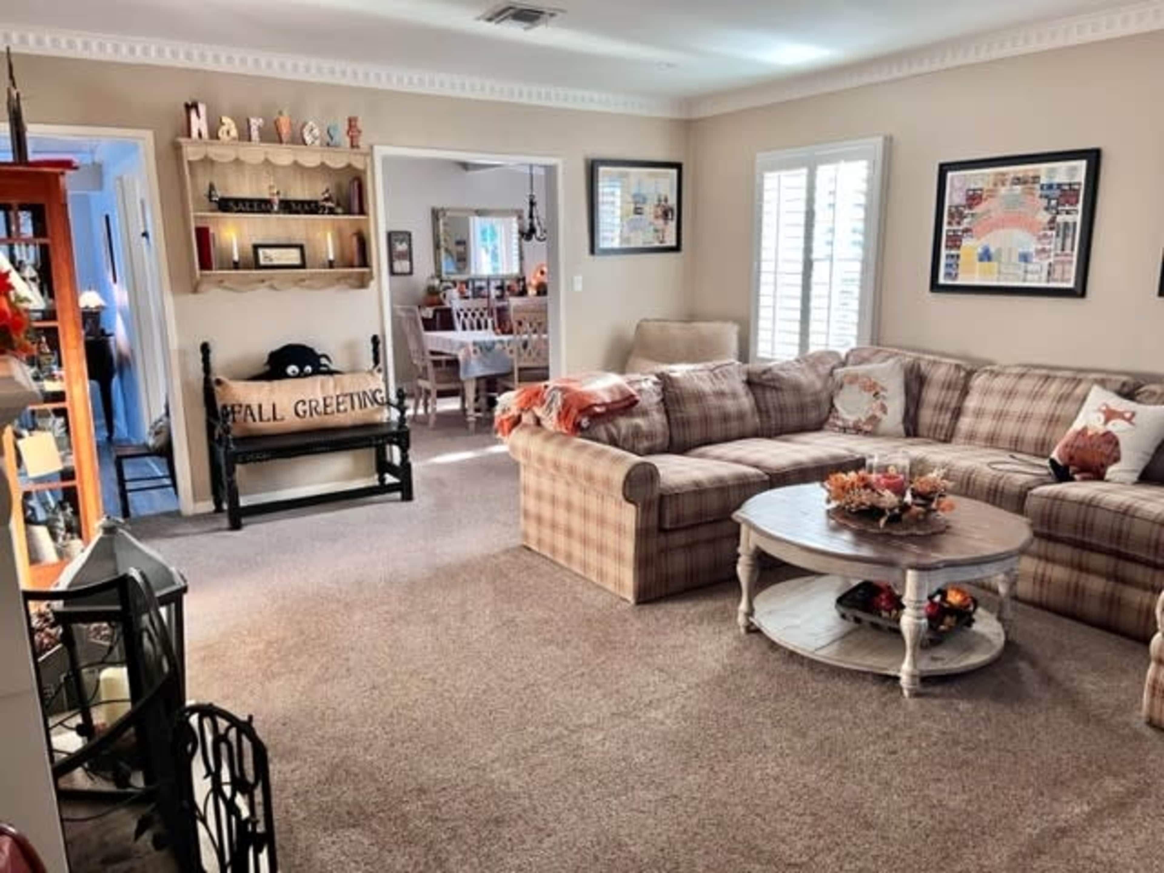 The photo shows a cozy living room featuring a plaid sectional sofa, a round coffee table with decorative items, and framed artwork on the walls.