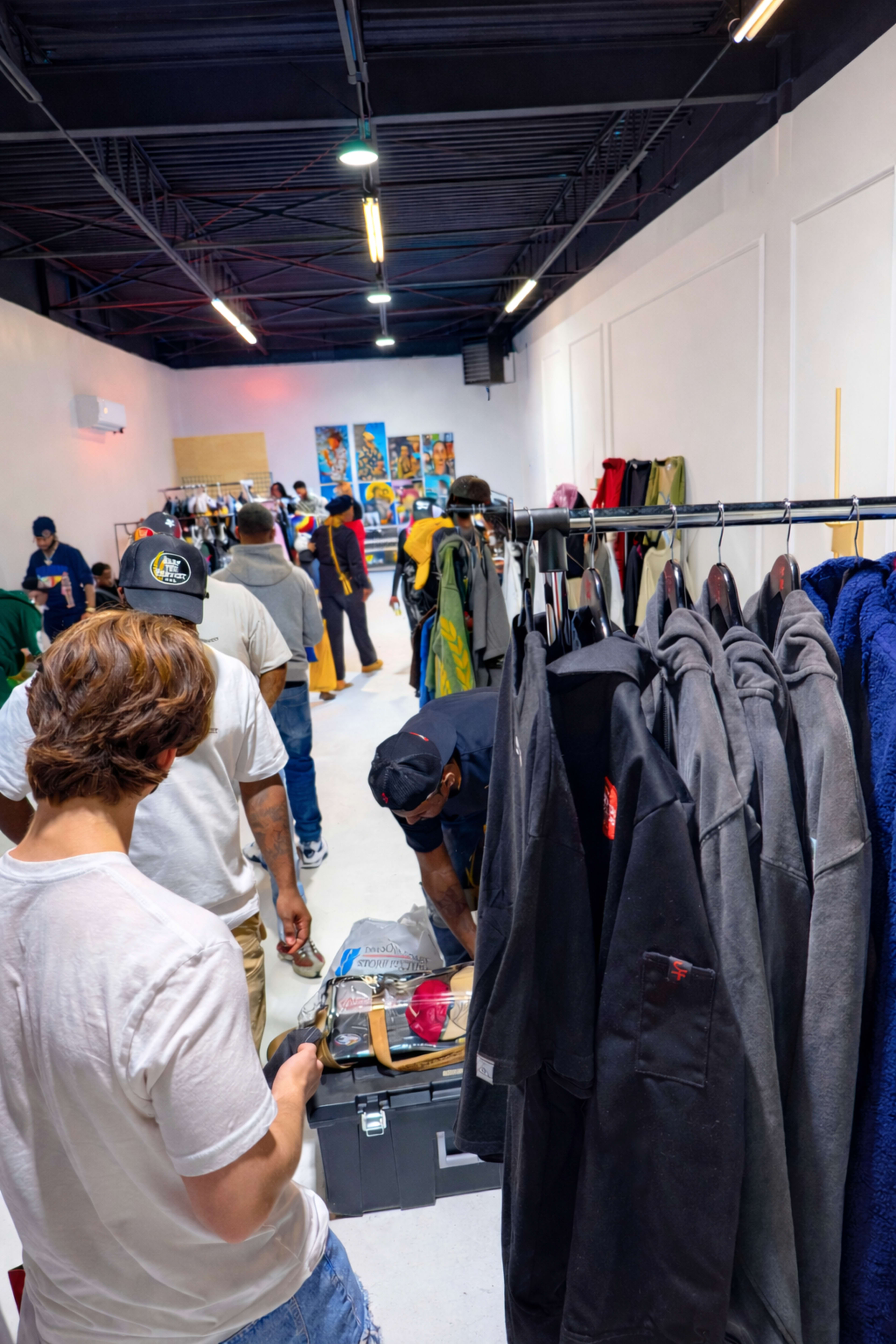 A clothing store features customers browsing racks of garments while others examine items laid out on a table.
