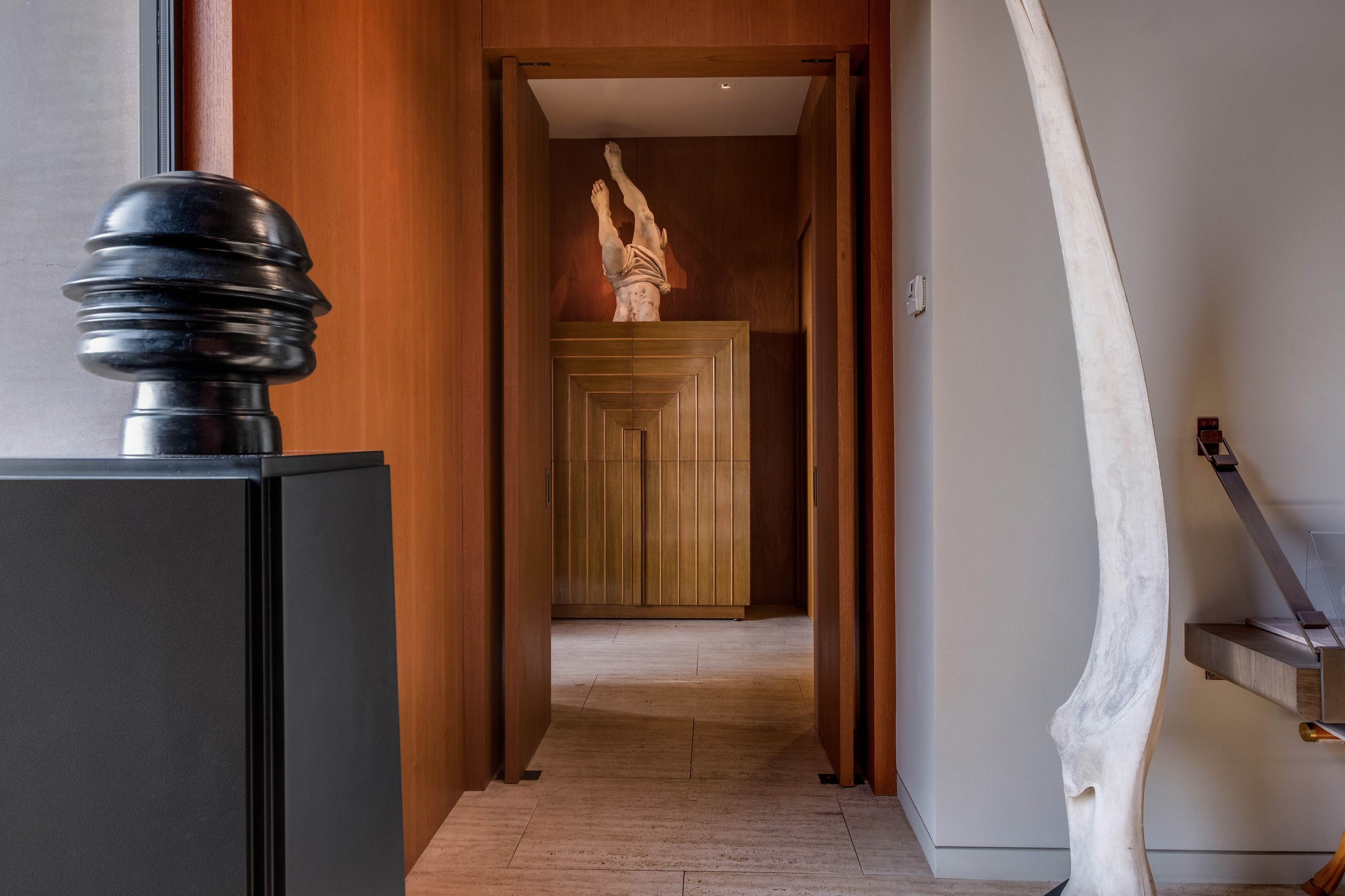 The image shows a hallway with a sculptural figure at the end, flanked by a tall, white, curved object and a black, rounded sculpture on the left.