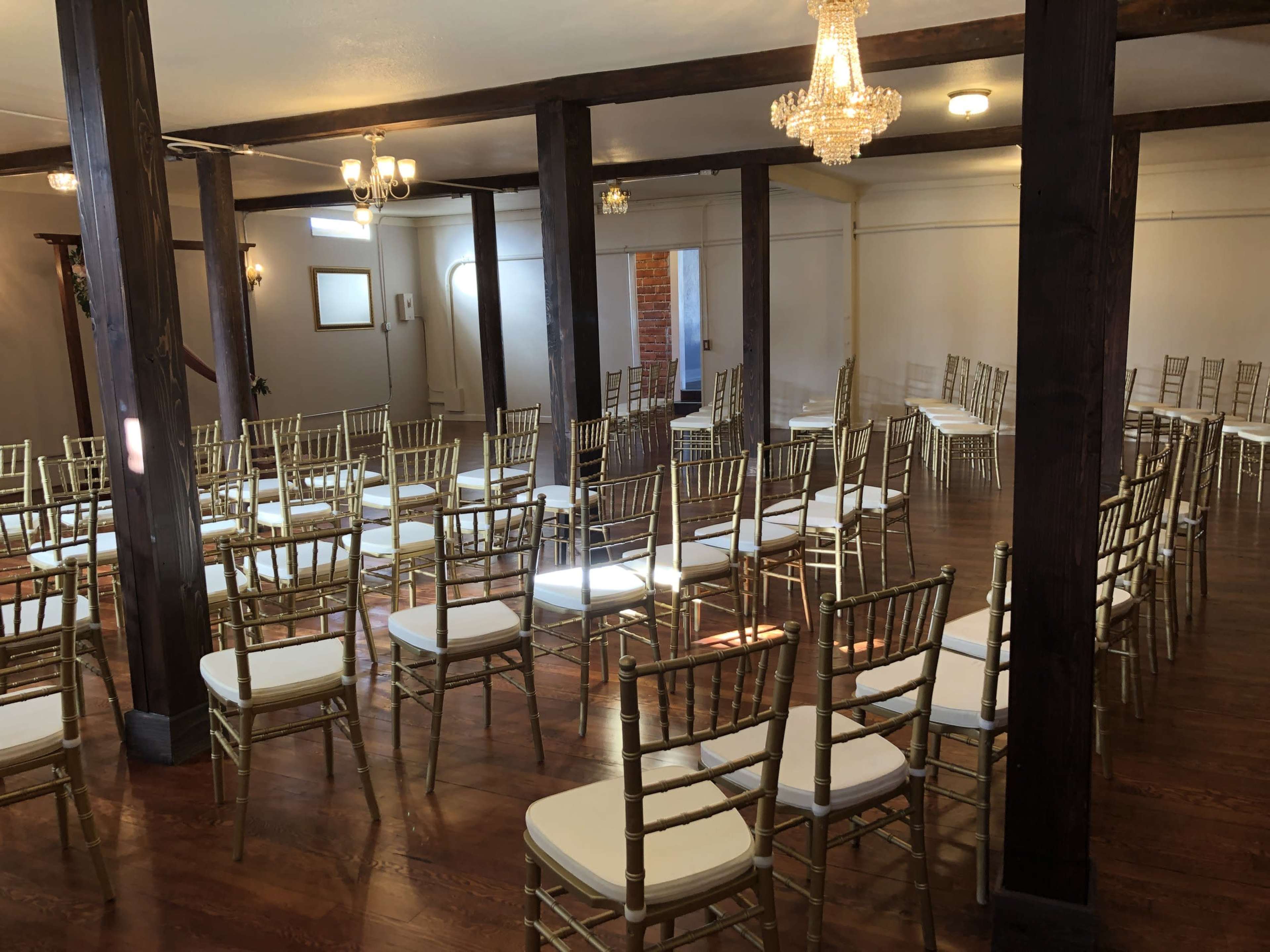 An empty event space features rows of gold chiavari chairs arranged on a polished wooden floor beneath chandeliers.
