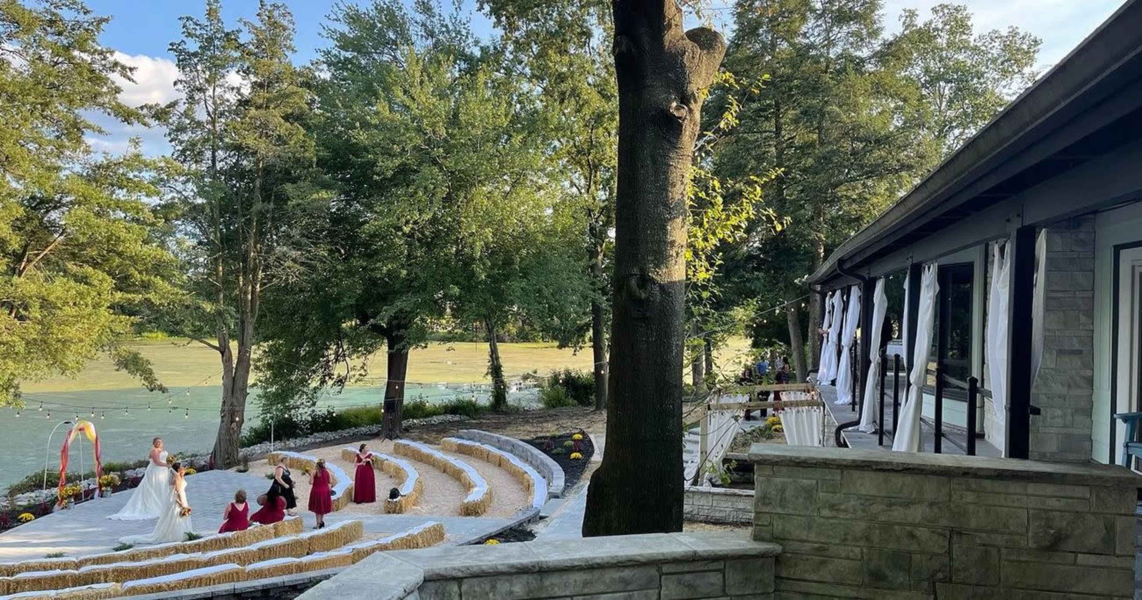 A wedding ceremony taking place in a circular seating area surrounded by trees, with a river visible in the background.