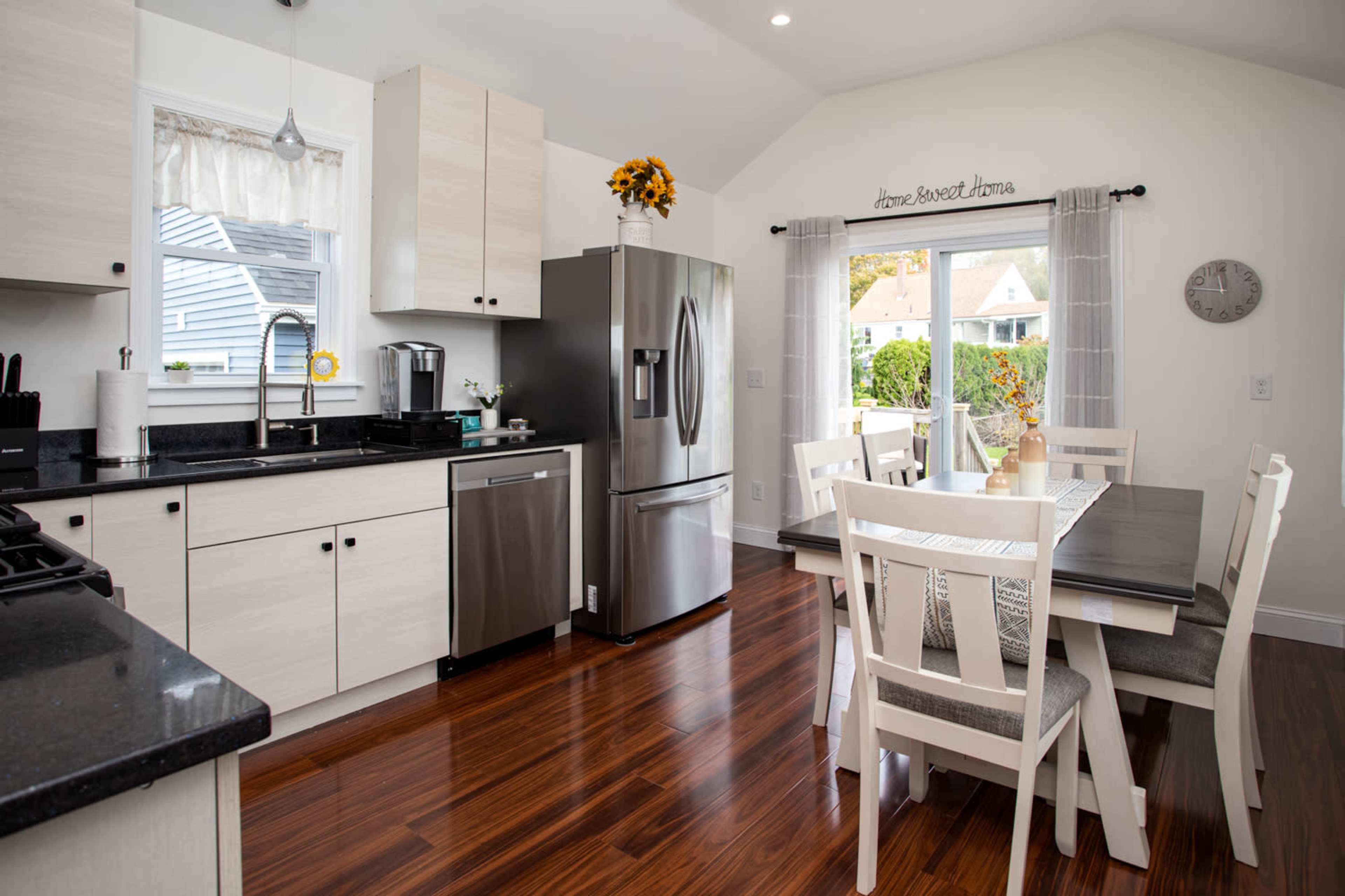 The kitchen features modern cabinetry, stainless steel appliances, and a dining table set for six against a backdrop of hardwood flooring.