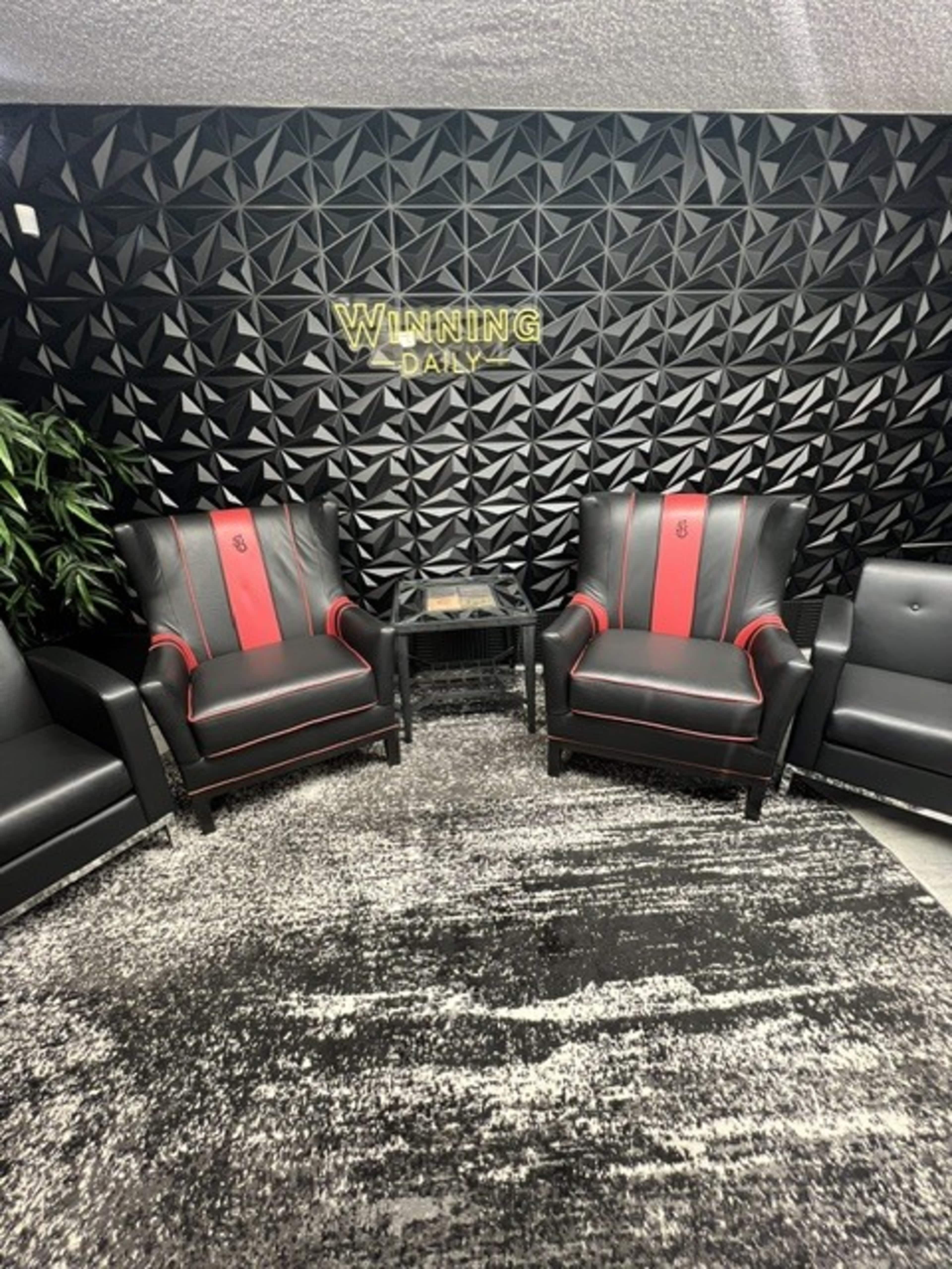 The image shows two black and red armchairs positioned in front of a textured black wall with the words "WINNING DAILY" displayed above them.