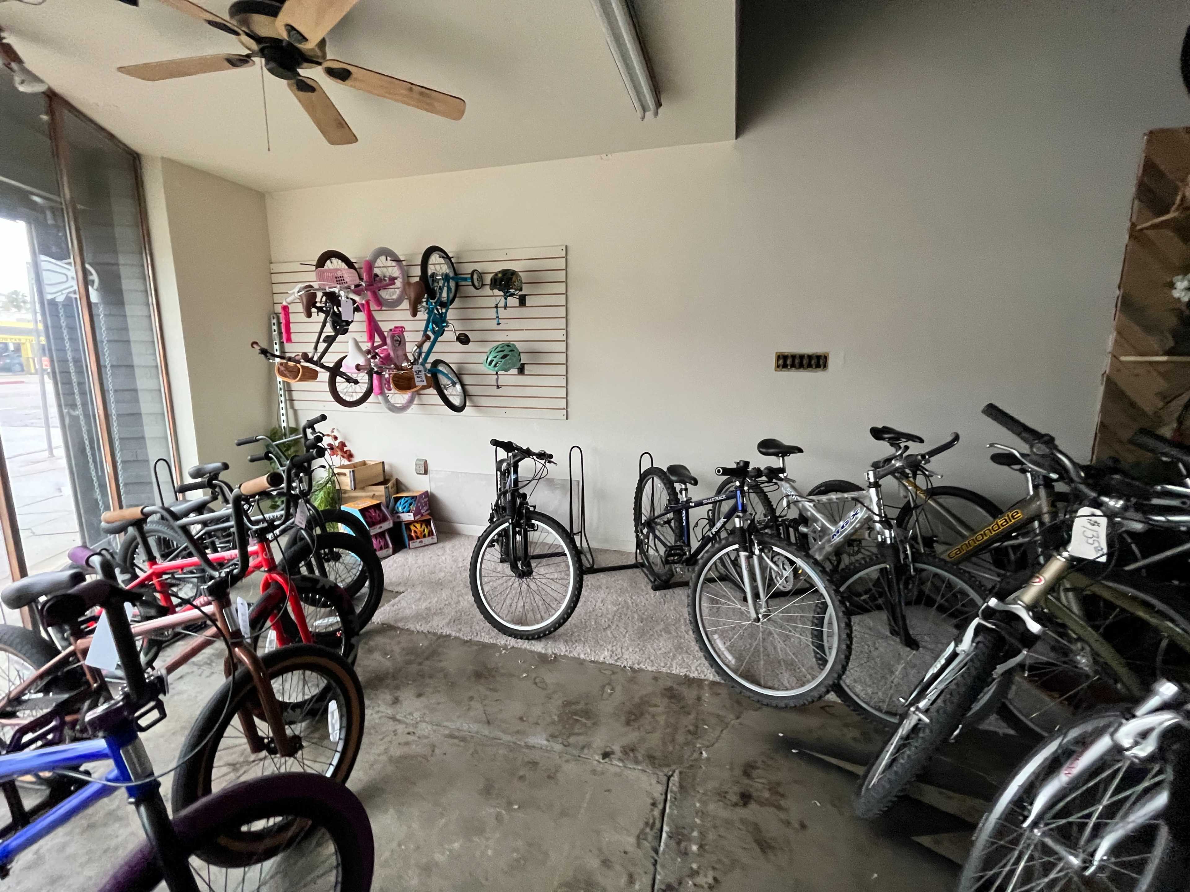 The image shows a bicycle shop with several bicycles parked on the floor and a wall displaying additional bikes and helmets.