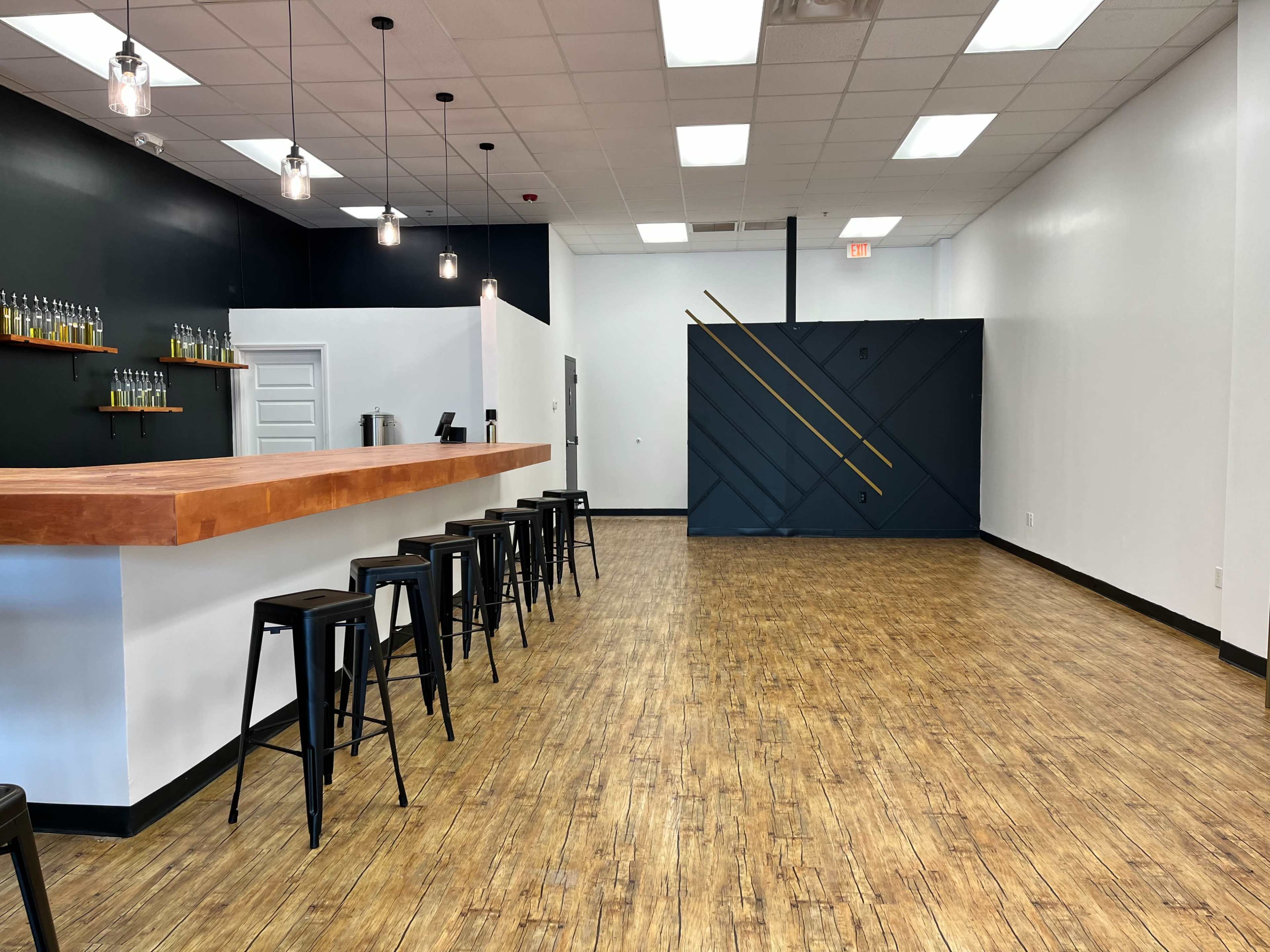 An empty interior of a modern bar or café with a wooden counter, black stools, and minimalistic decor featuring a geometric accent wall.