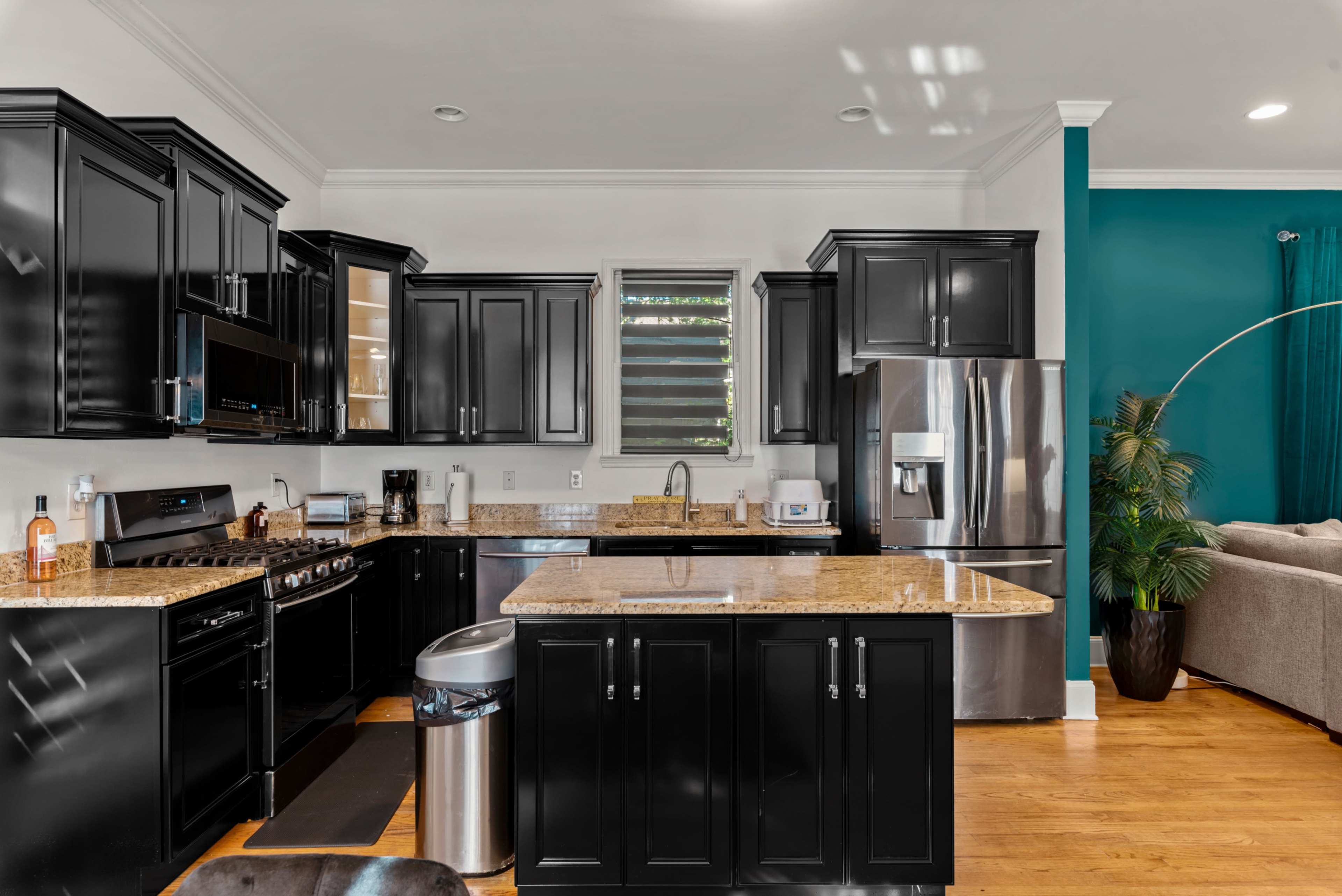 A modern kitchen with black cabinets, granite countertops, stainless steel appliances, and an island with a trash bin.