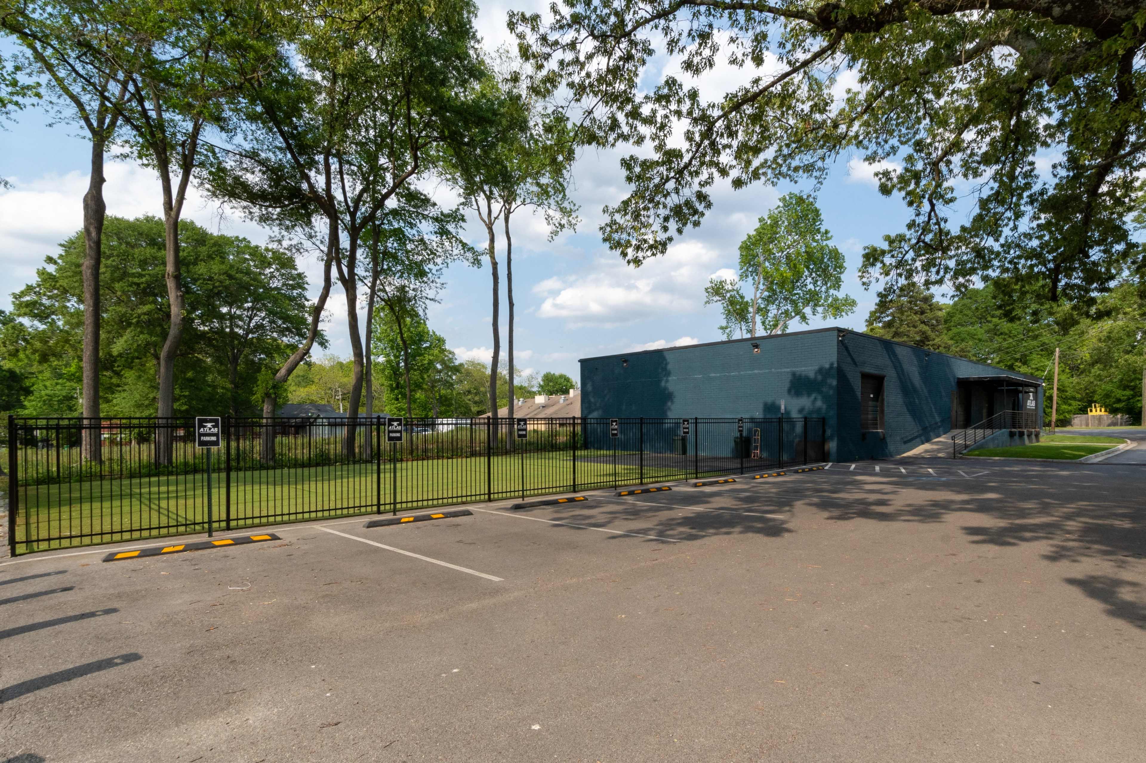 A dark blue building surrounded by trees, with a gated entrance visible from a paved parking lot.