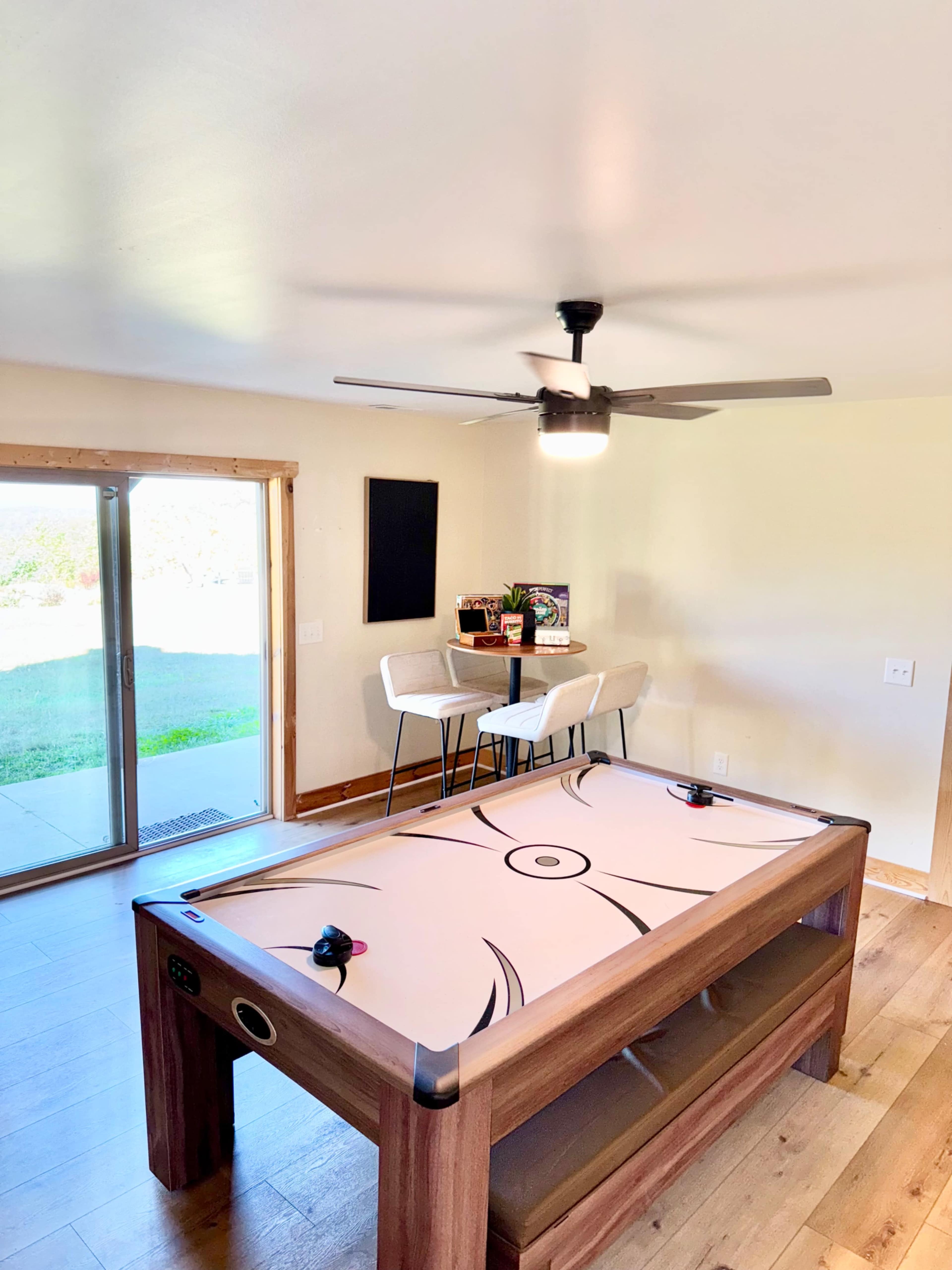 The image shows a room with a pool table, a dining table with two chairs, a ceiling fan, and a sliding glass door that opens to an outdoor area.