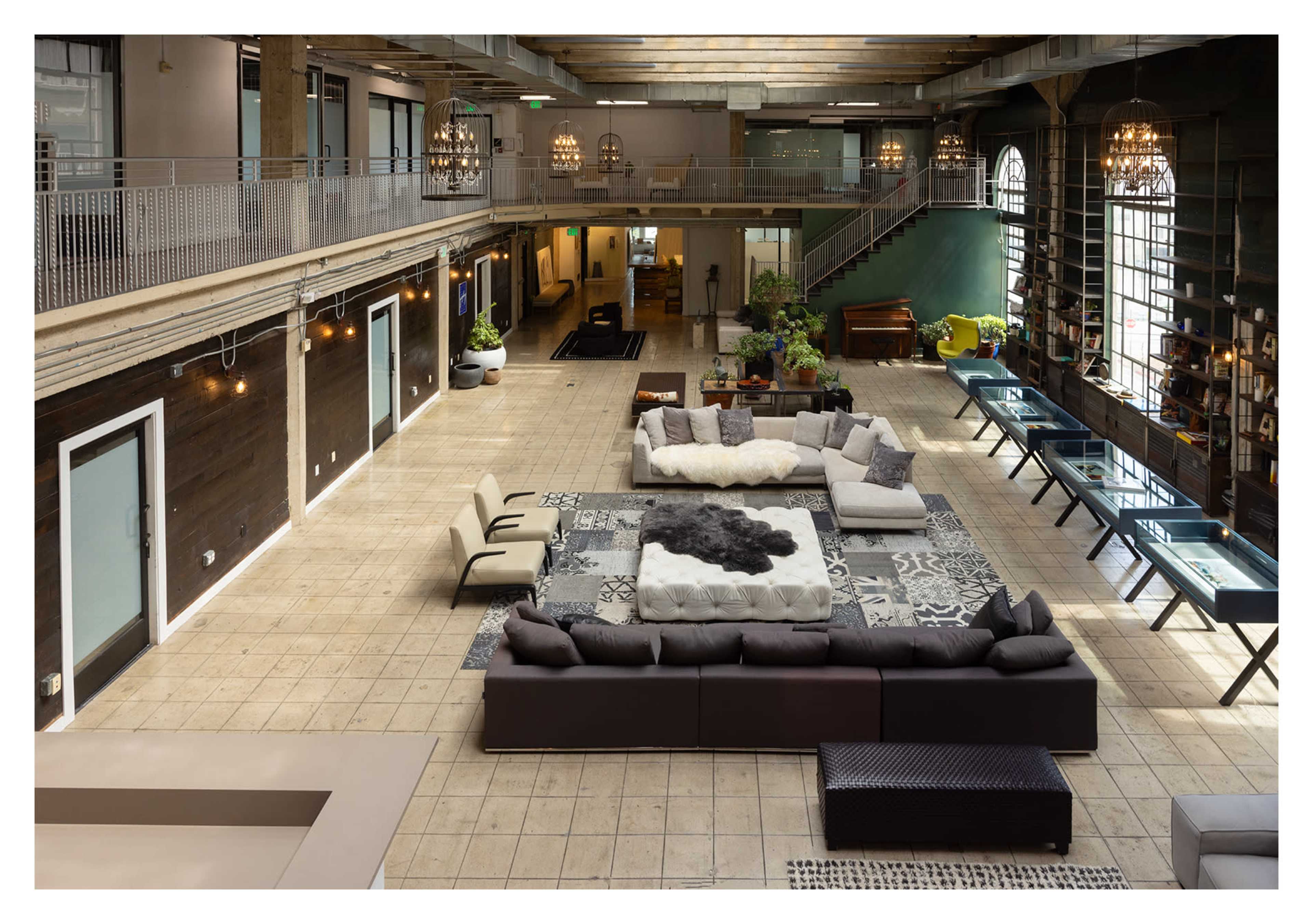 The image showcases a spacious, open-concept lounge area with modern furniture arrangements, large windows, and decorative plants, situated within a well-lit interior featuring high ceilings.