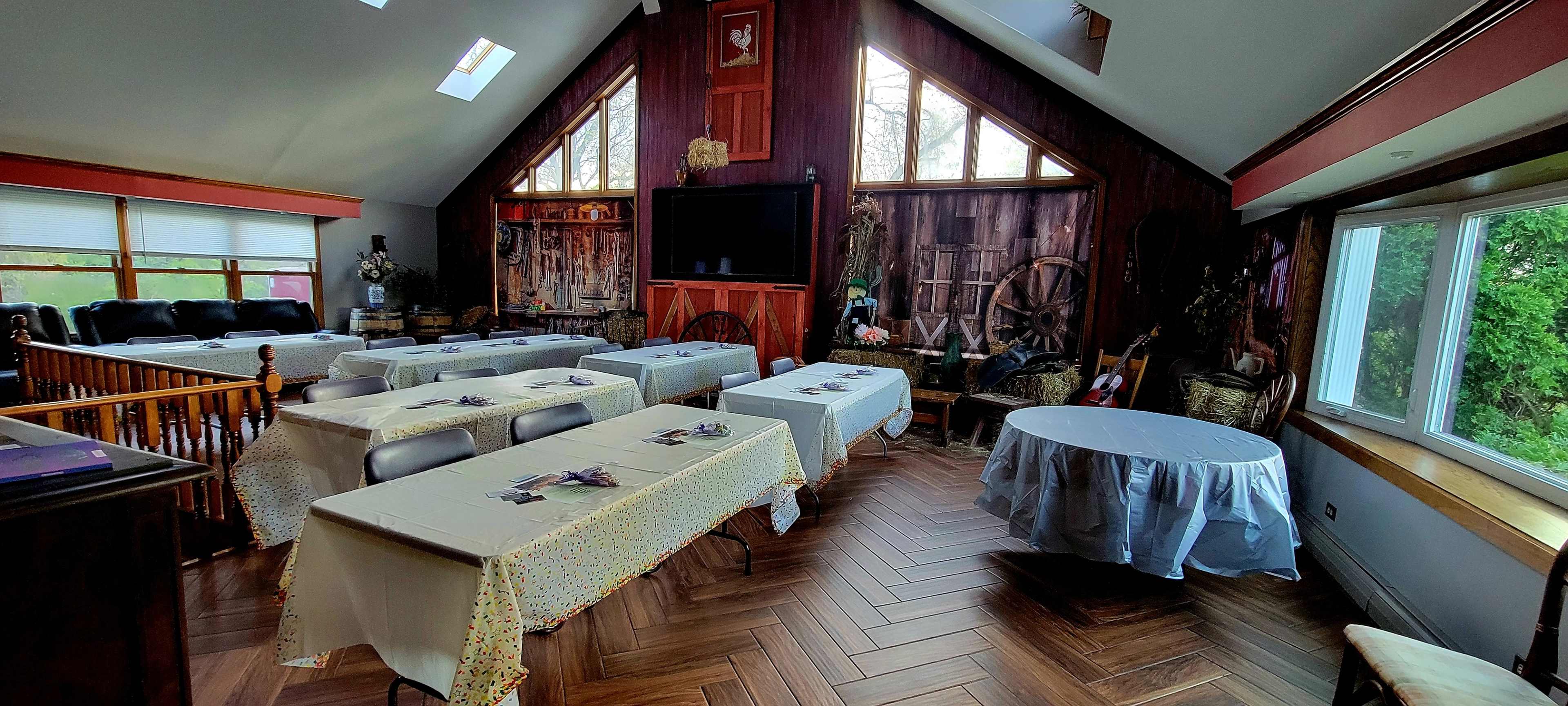 A spacious, rustic-looking room set up with several tables covered in white tablecloths, arranged for an event.