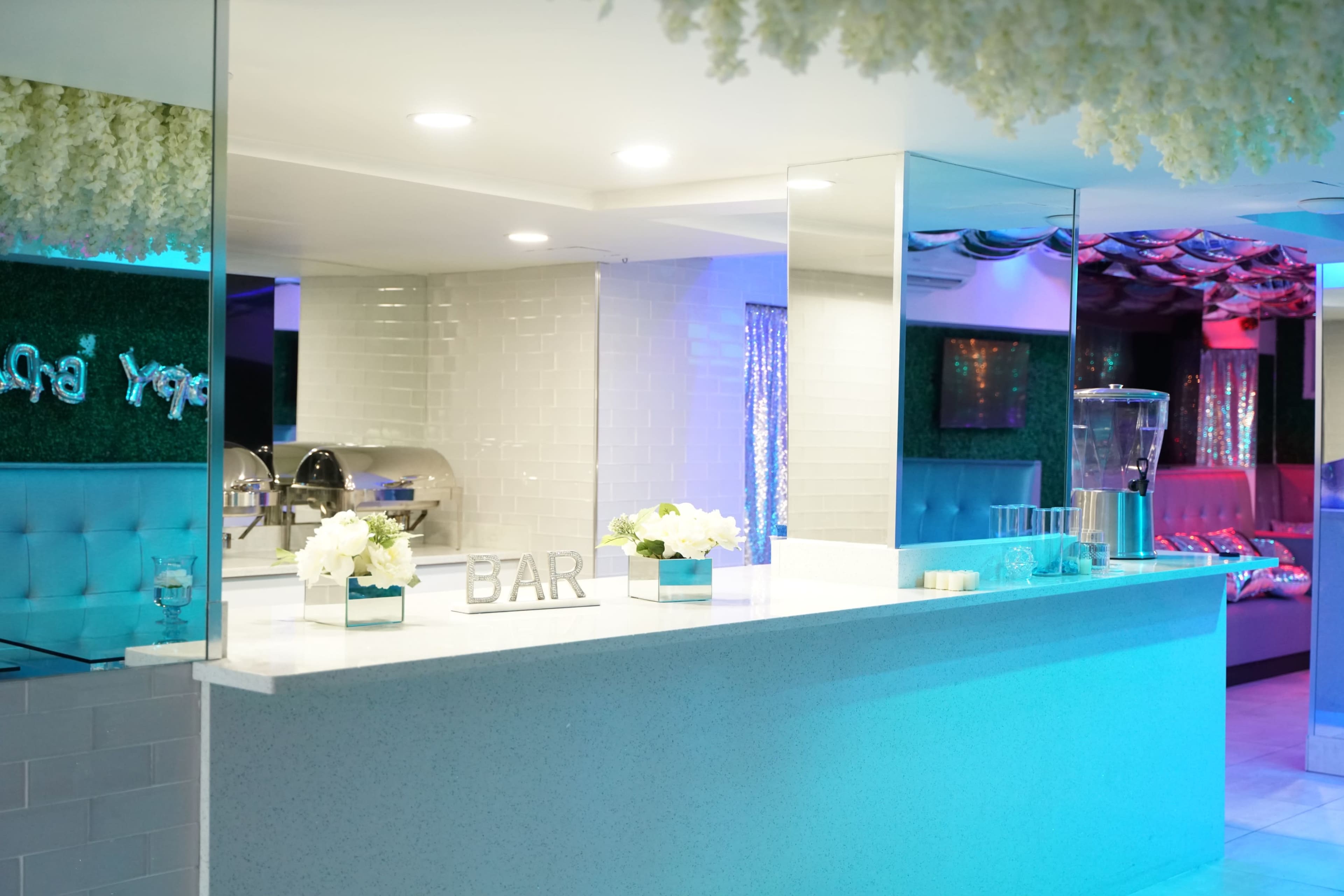 A modern bar area with a white counter, floral arrangements, and colorful lighting in a stylish interior.