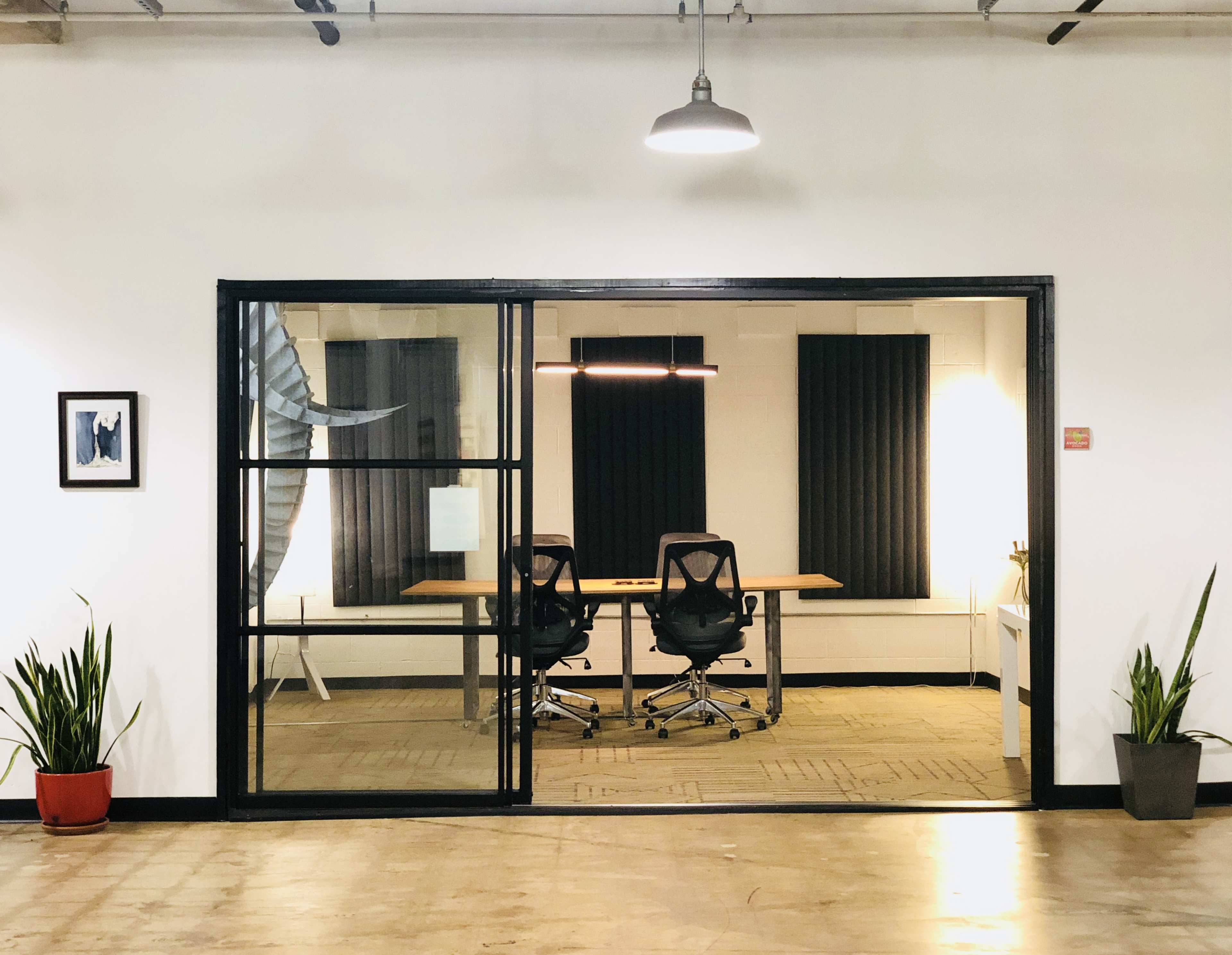 A sleek office space features a glass door entry leading to a room with two chairs, a long table, and black window coverings.