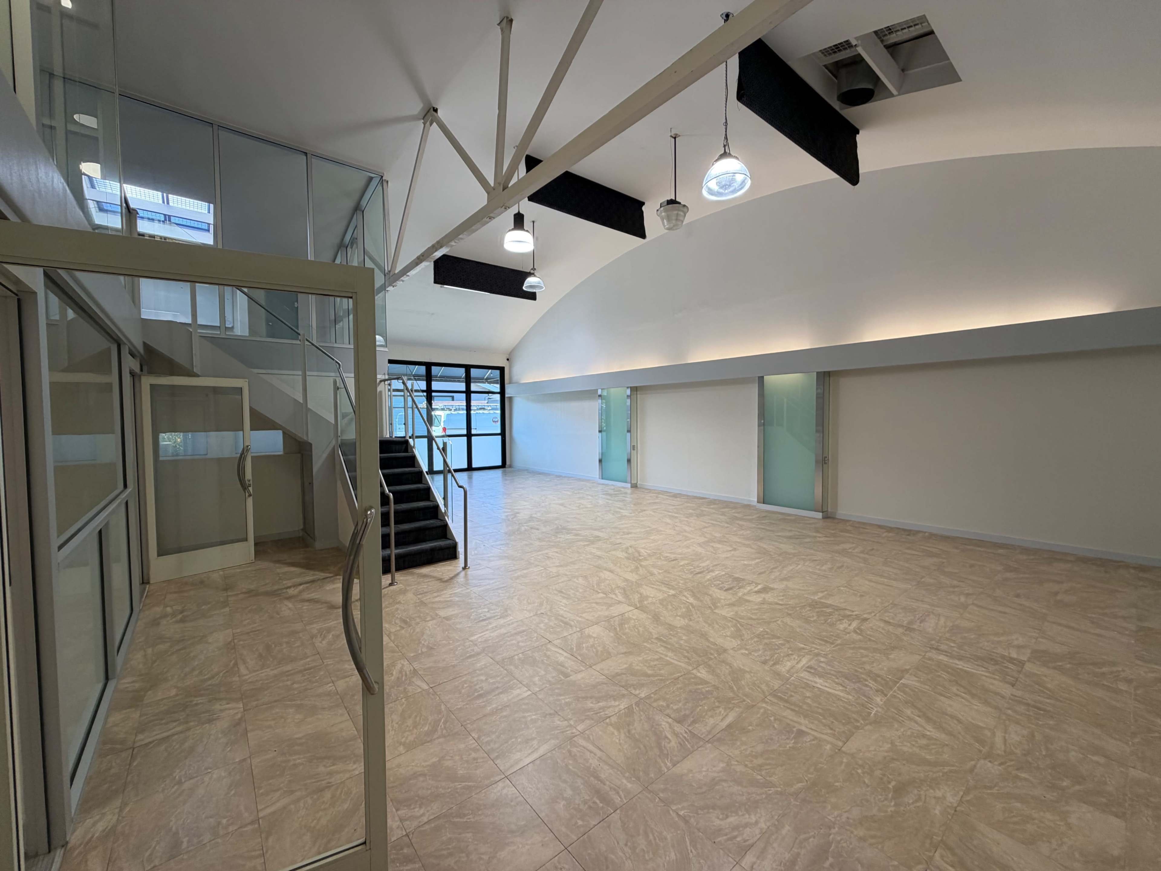 The image shows a spacious, modern interior of an office or commercial space with large windows, a staircase, and a polished floor.