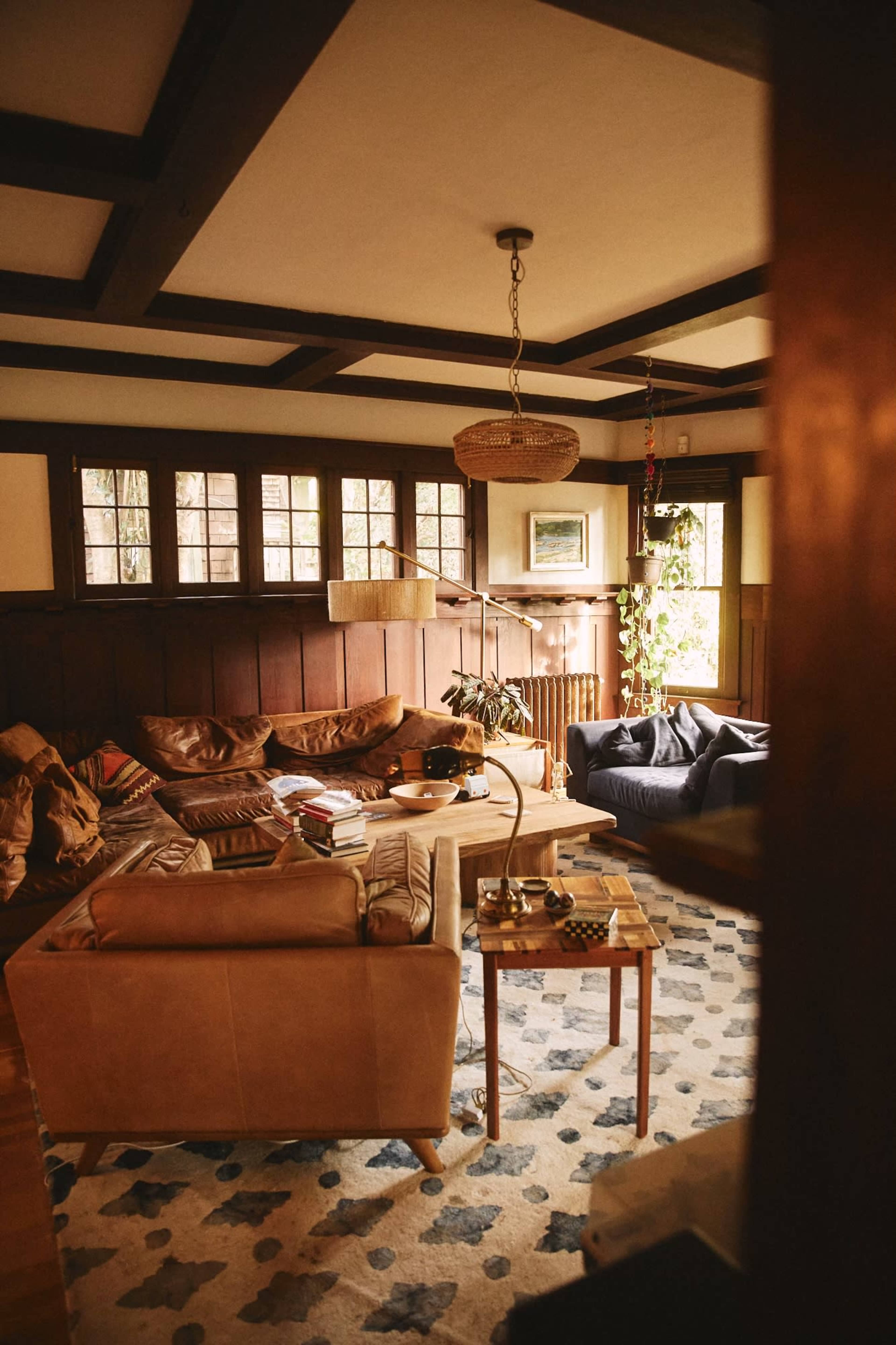 A cozy living room with a mix of leather and fabric seating arranged around a coffee table, featuring wooden walls and large windows letting in natural light.