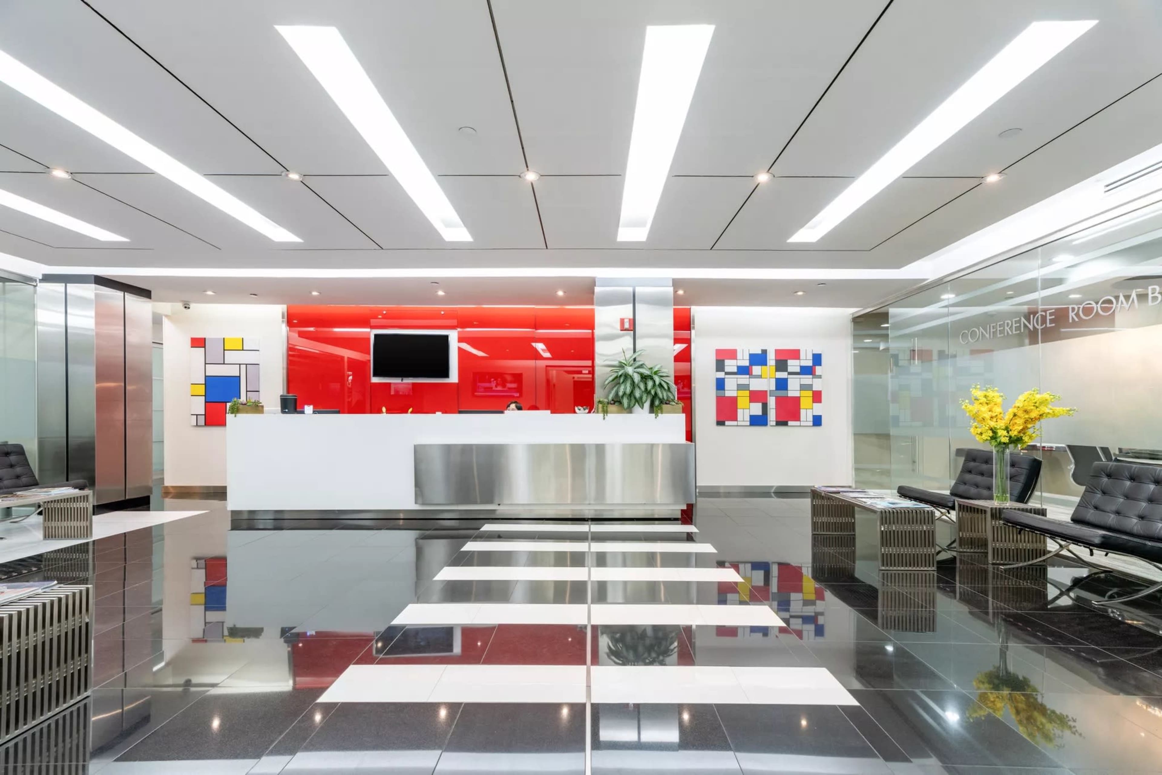 The image shows a modern reception area with a sleek front desk, vibrant wall art, and contemporary seating arrangements.
