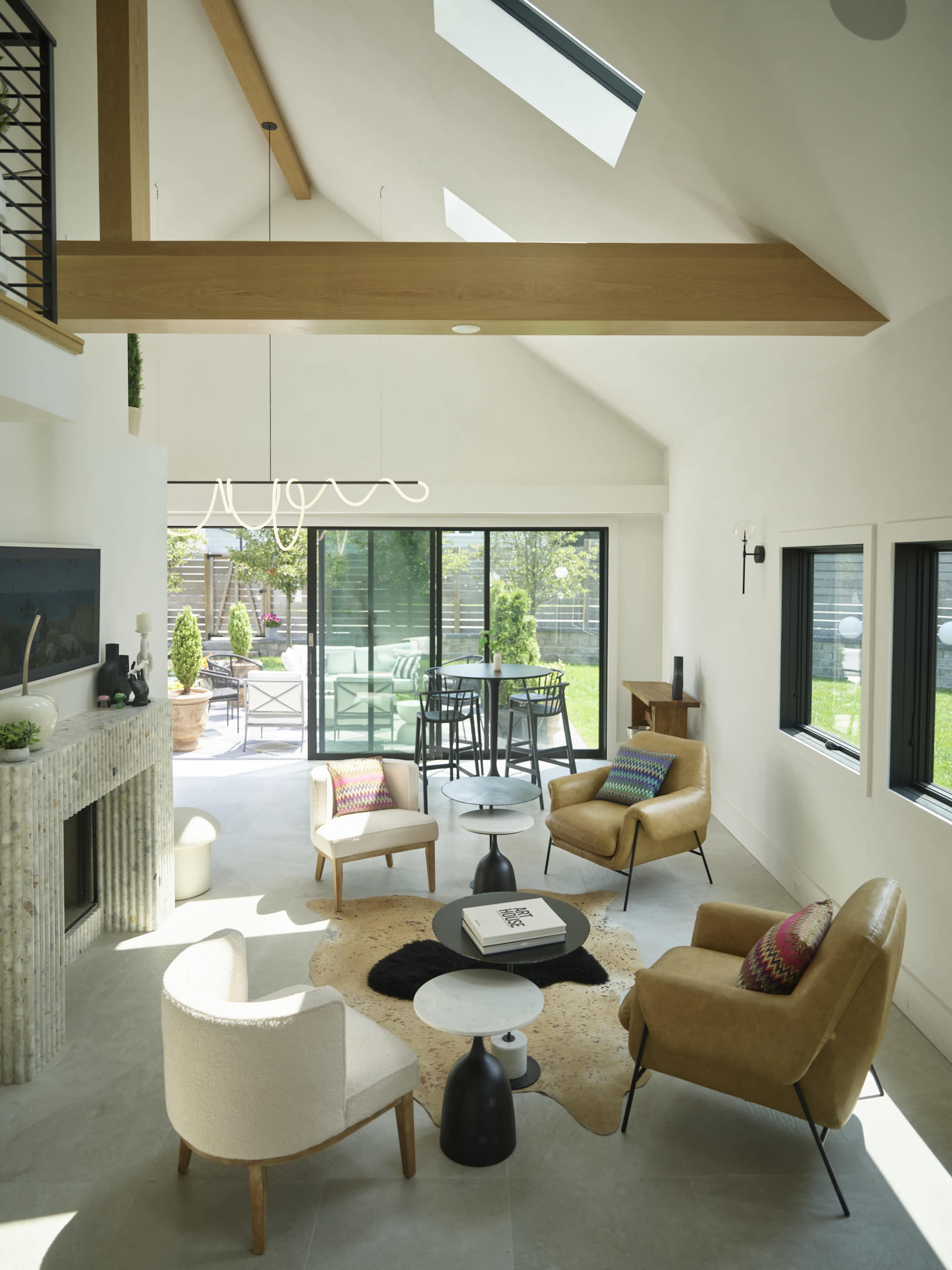 The room features a modern open layout with high ceilings, large windows, and a mix of seating arrangements surrounding a central coffee table.