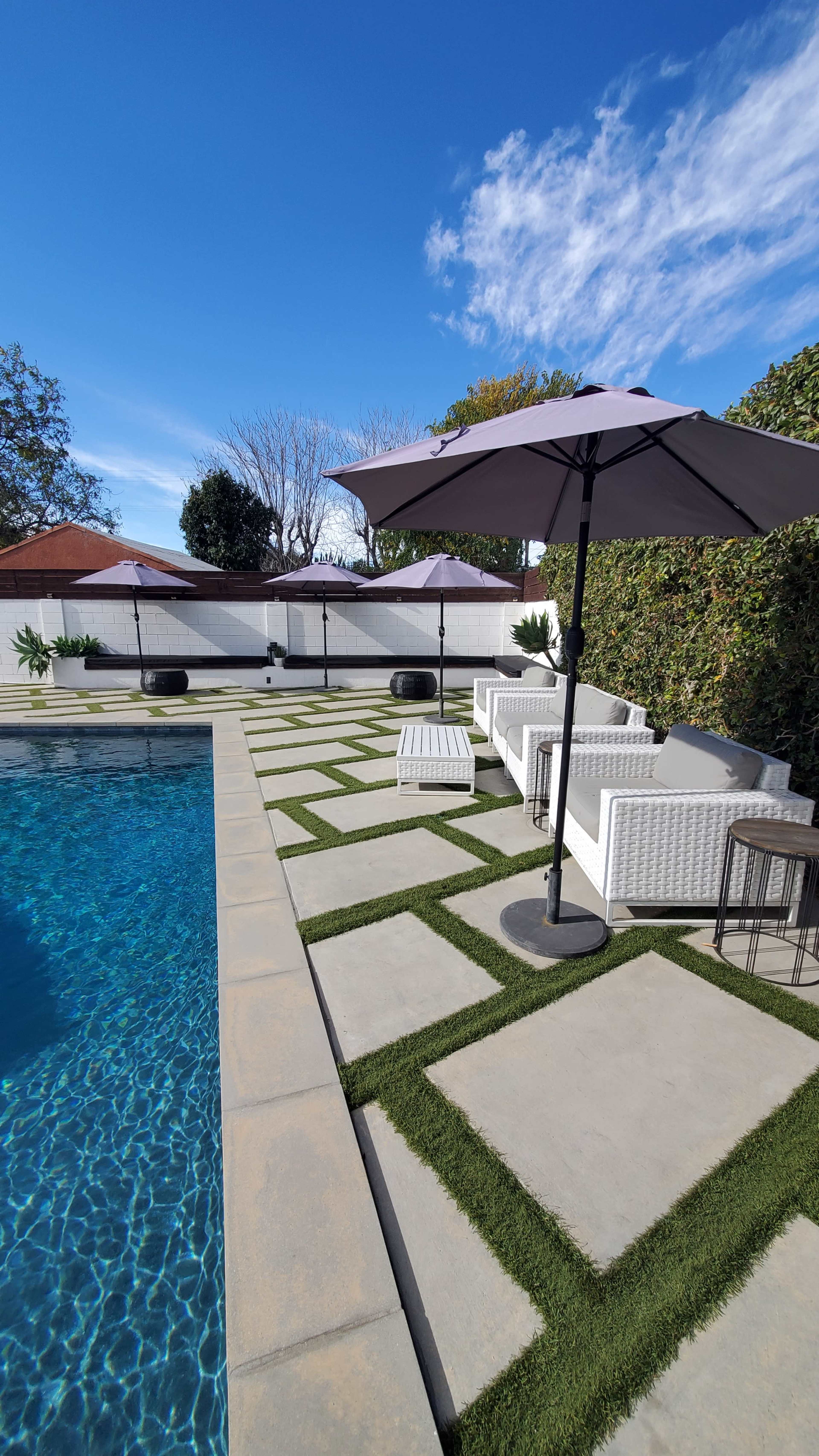The image shows a well-maintained pool area featuring lounge chairs, umbrellas, and decorative landscaping.