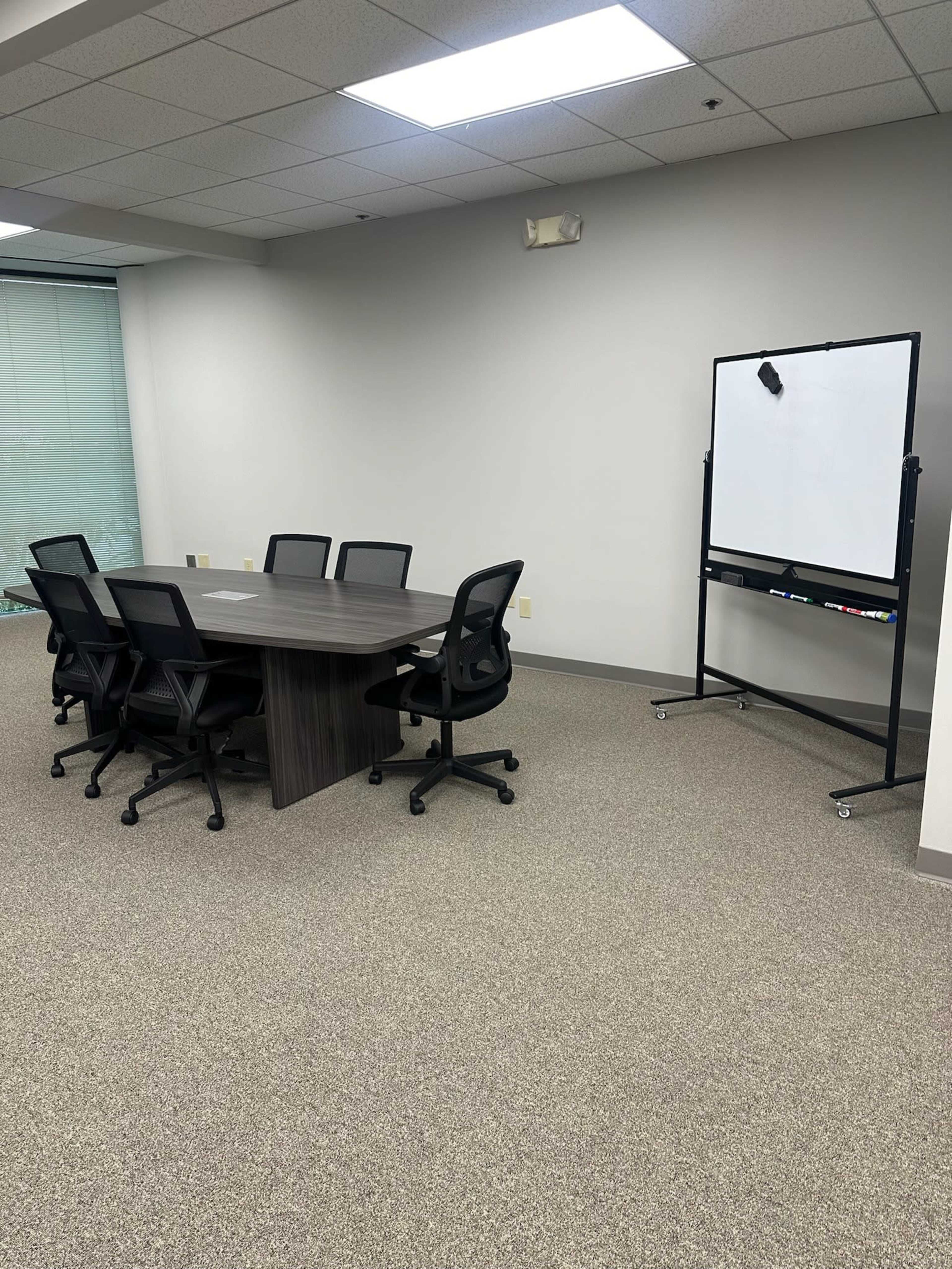 A conference room features a rectangular table surrounded by six mesh chairs and a mobile whiteboard on wheels.