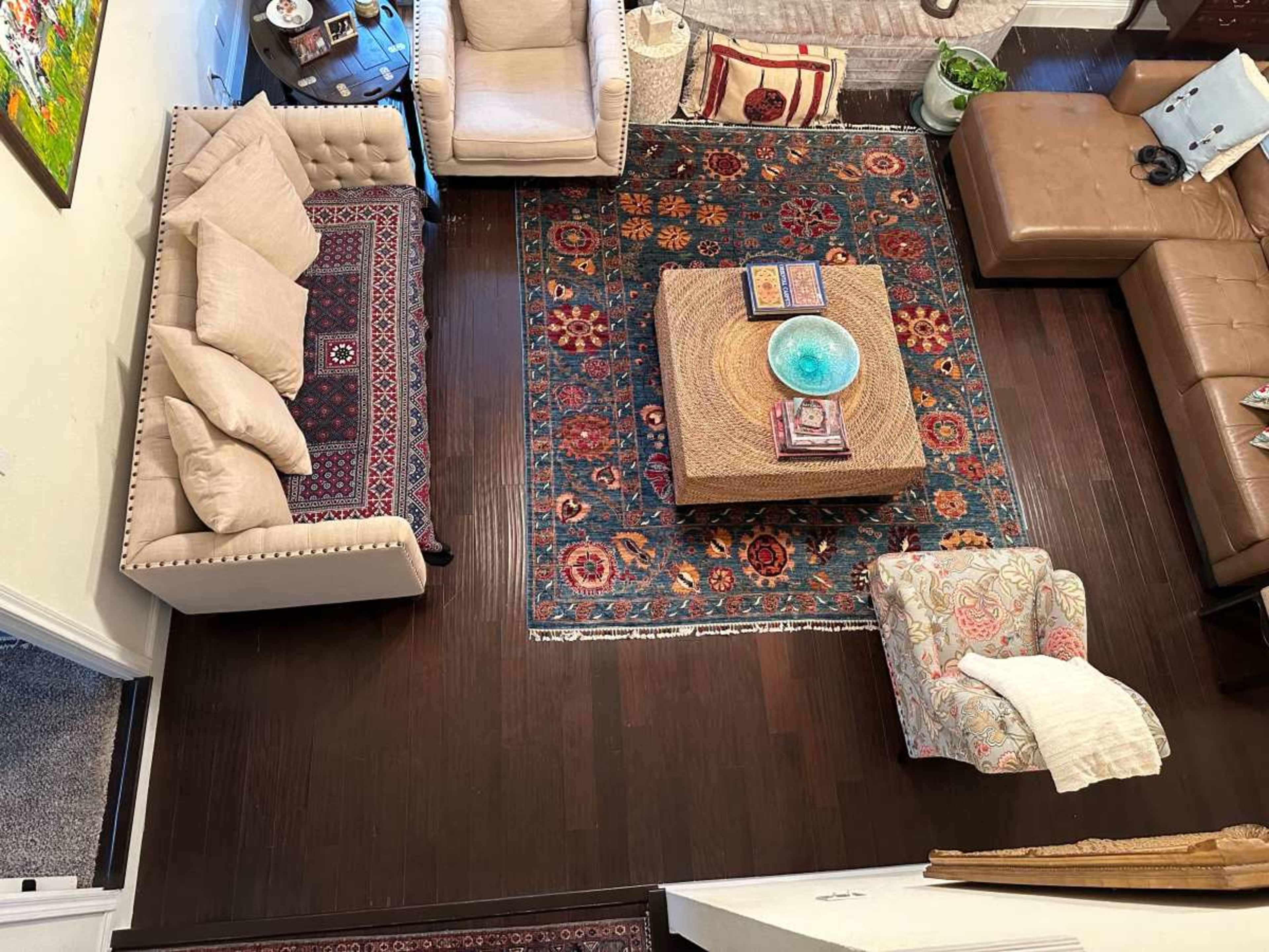 The image shows a living room with a patterned area rug, a coffee table, and various seating arrangements, including a beige sofa and armchair.