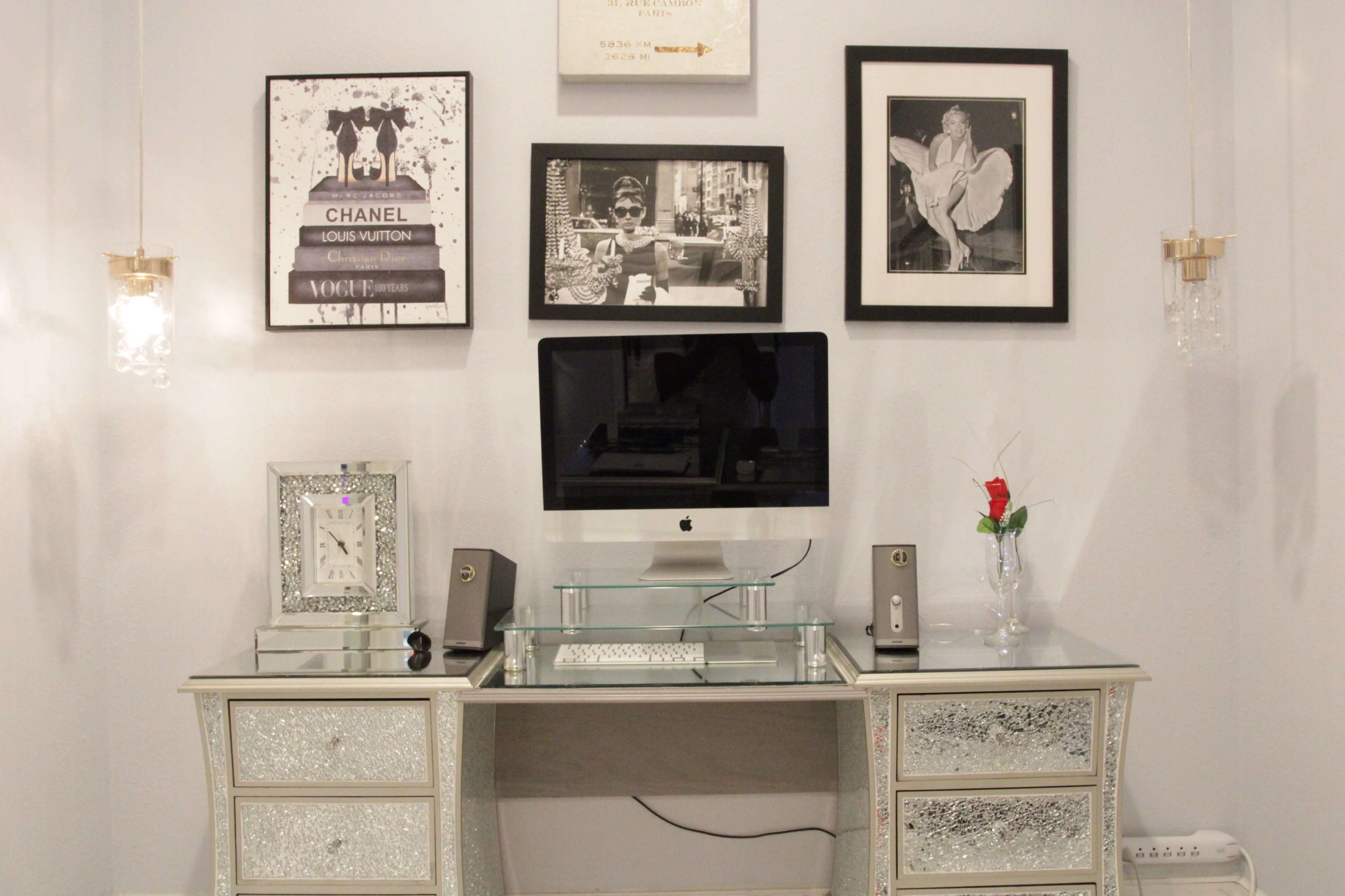 A modern desk setup with an iMac, decorative picture frames on the wall, and mirrored furniture.