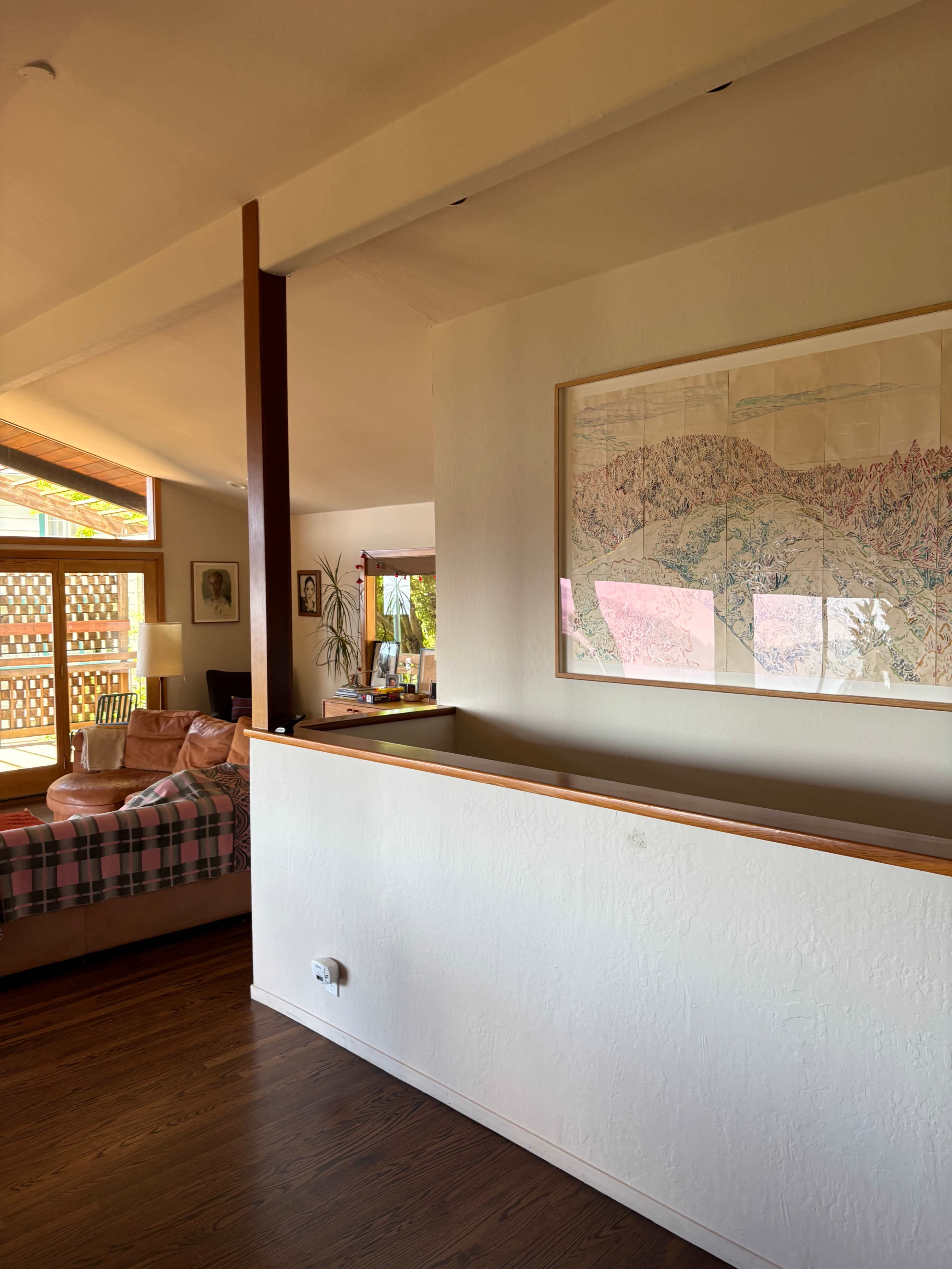 The image shows a spacious interior of a home with a sectional sofa, large windows, and a framed map artwork on the wall.