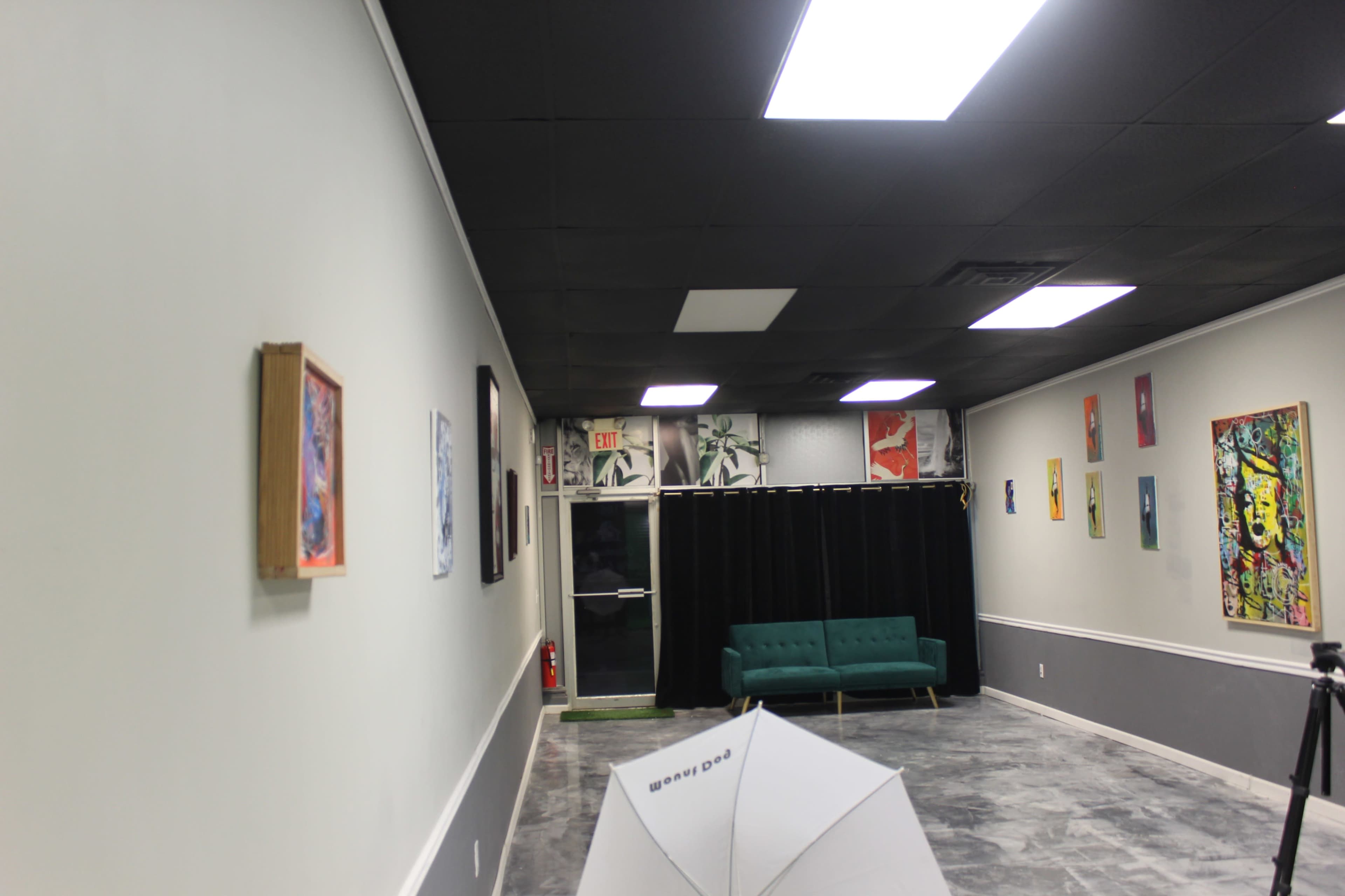 The image shows a well-lit art gallery with a green couch, colorful artwork on the walls, and a curtain at the back.