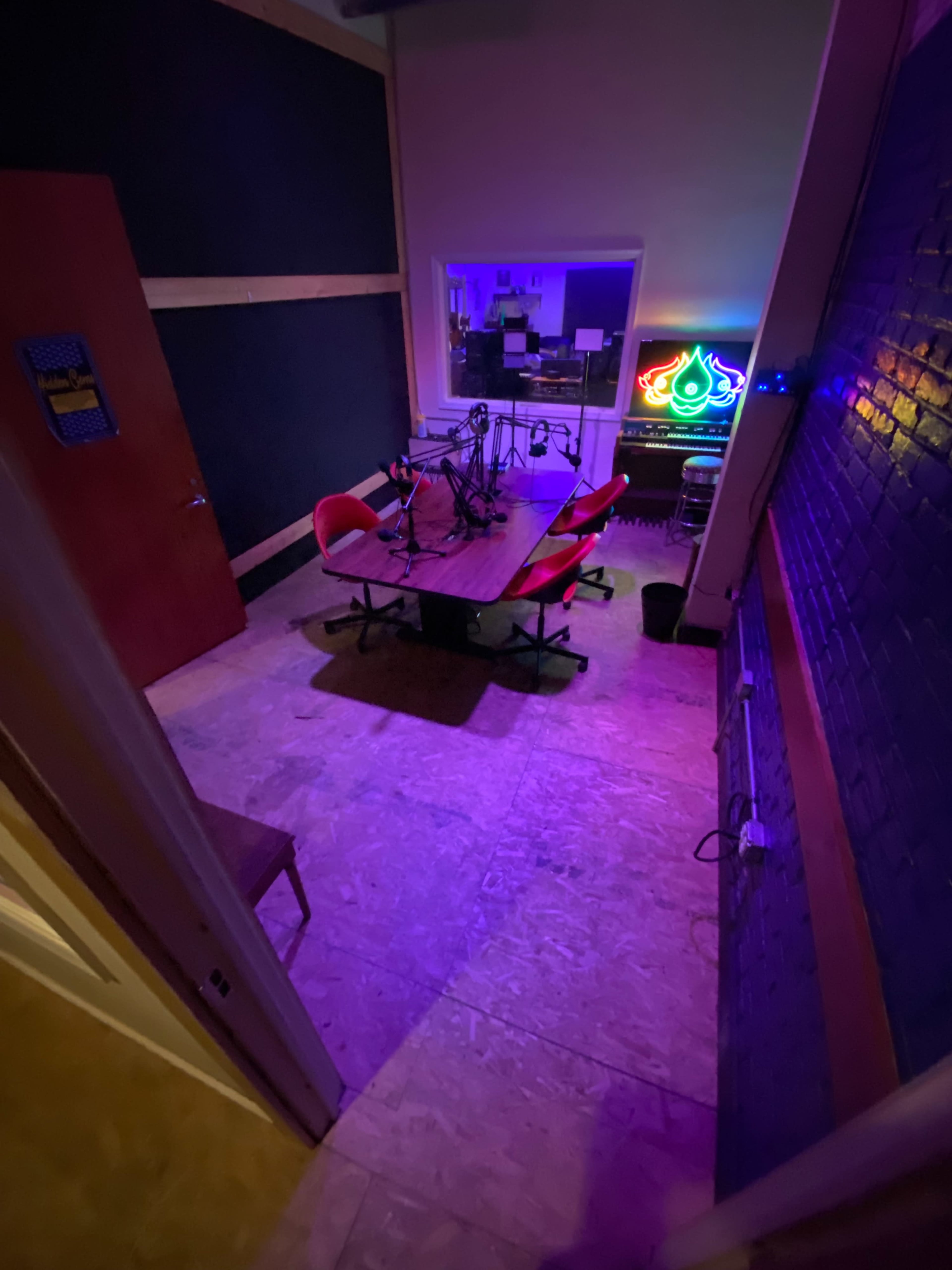 A recording studio with a table, microphones, and four red chairs under purple lighting.