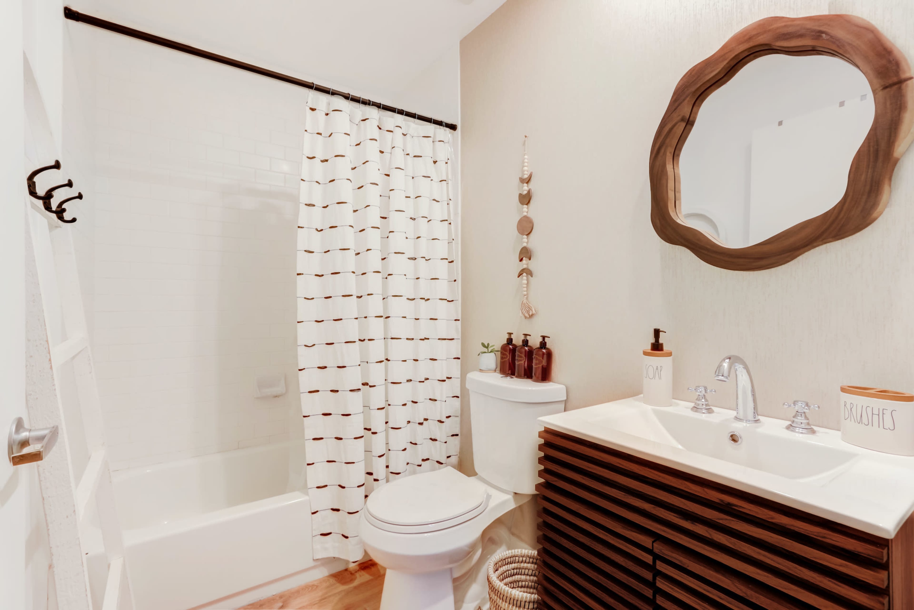 The bathroom features a shower-tub combination, a modern vanity with a sink, and a large mirror, complemented by a patterned curtain and wood accents.