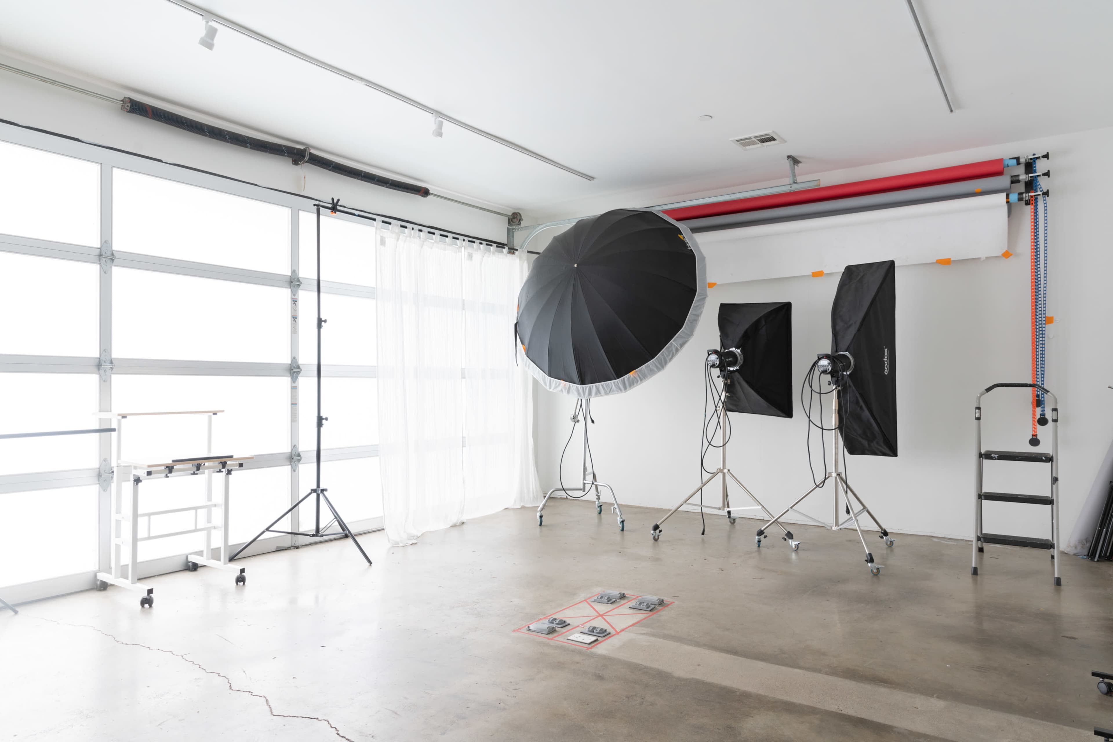 A photography studio features large softbox lights, a backdrop system, and a simple cart in a spacious, well-lit room.