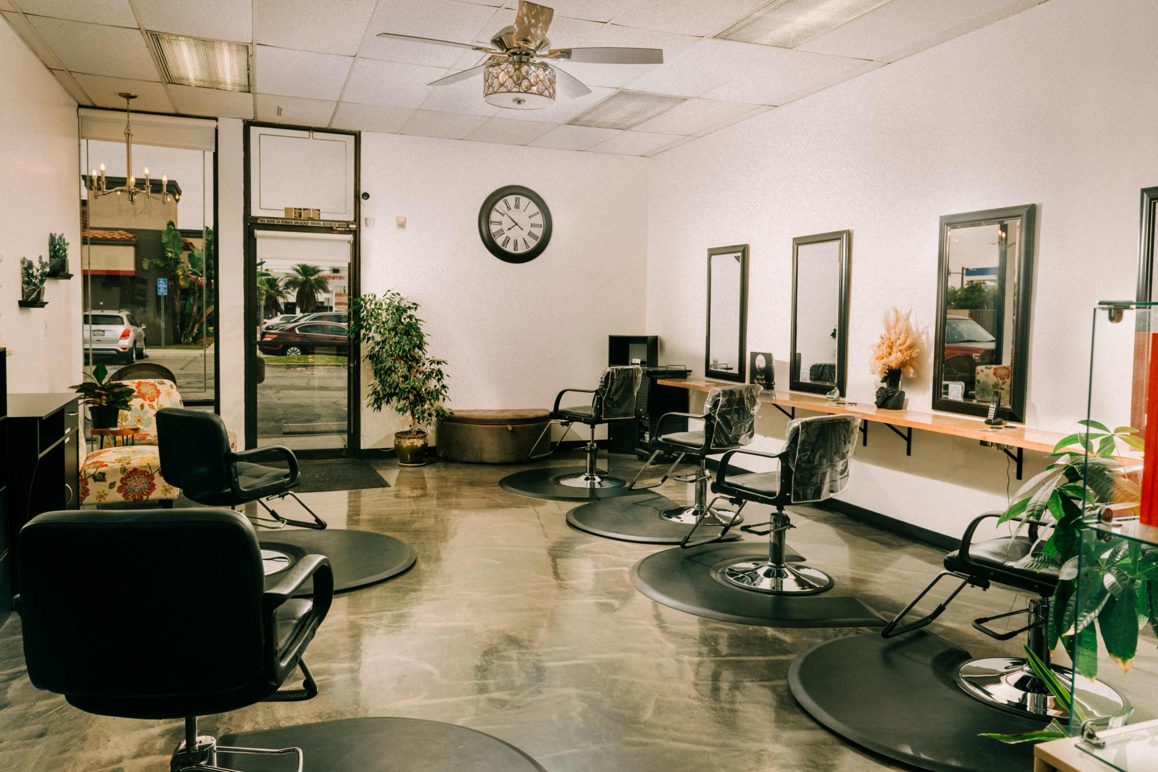 The image shows a hair salon interior with several styling chairs, mirrors, and a large window allowing natural light to enter.