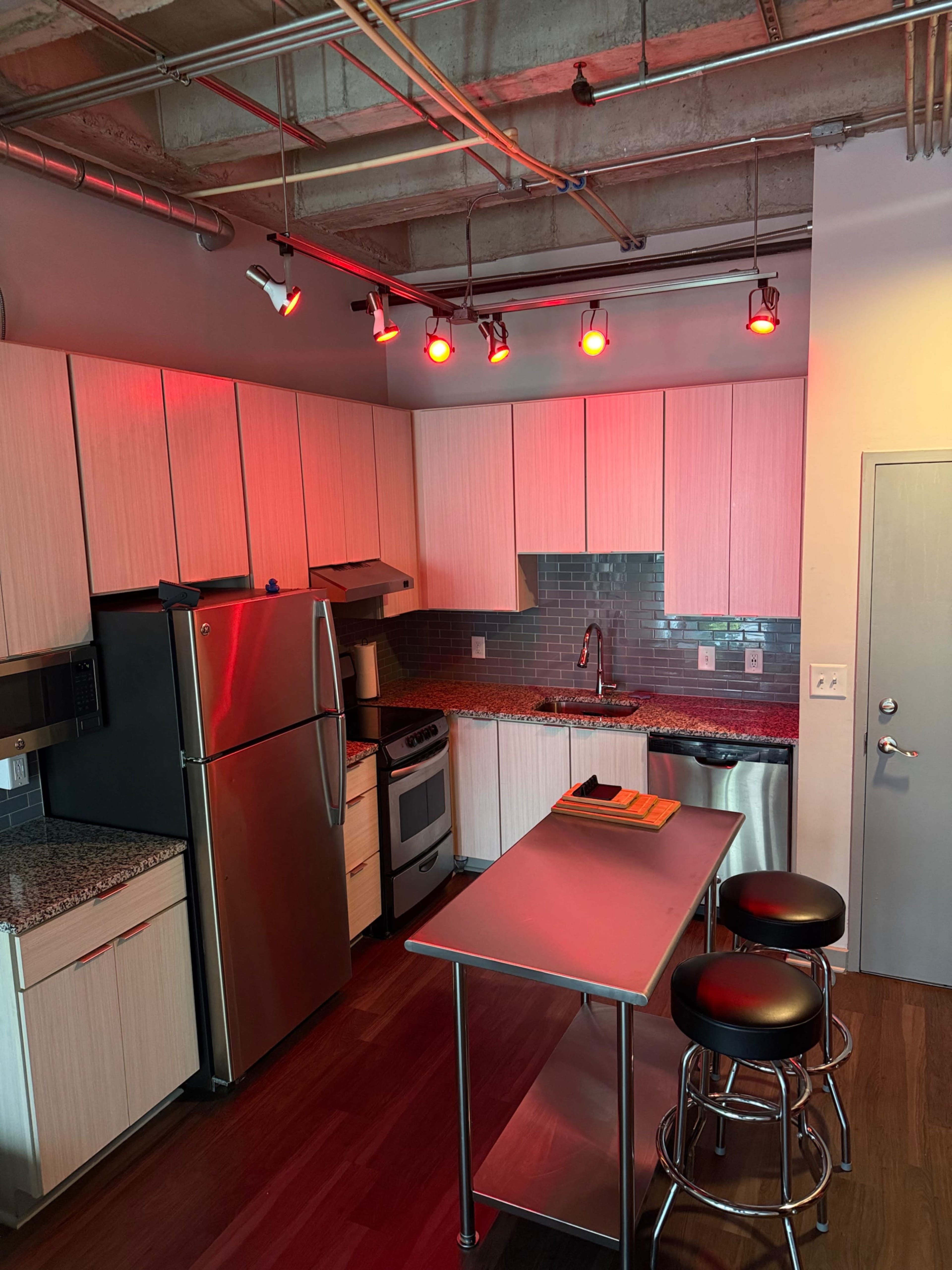 The image shows a modern kitchen with stainless steel appliances, a dark countertop, and pendant lighting.