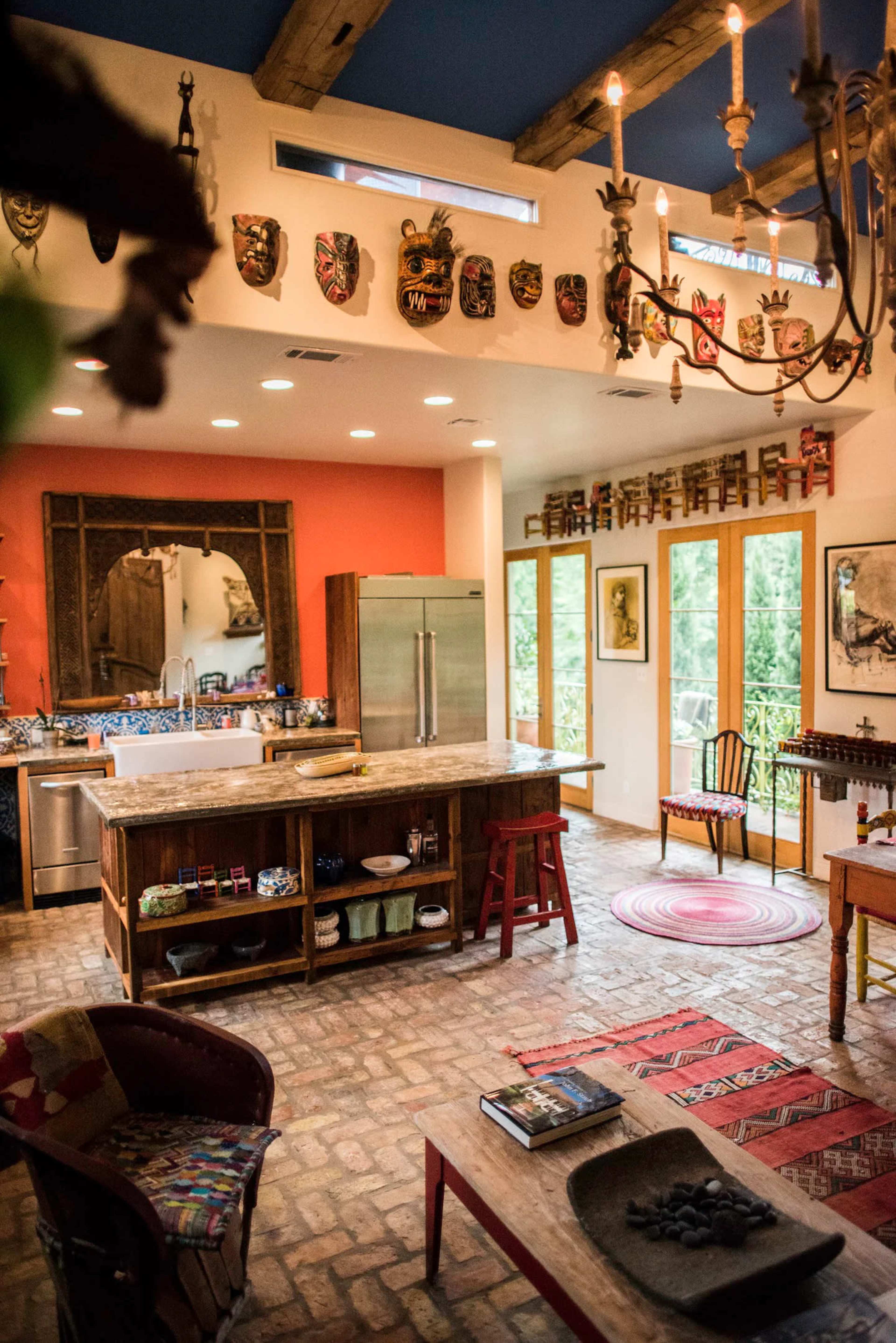 The image shows a spacious kitchen and dining area featuring a large island, wooden furniture, and decorative masks on the walls.