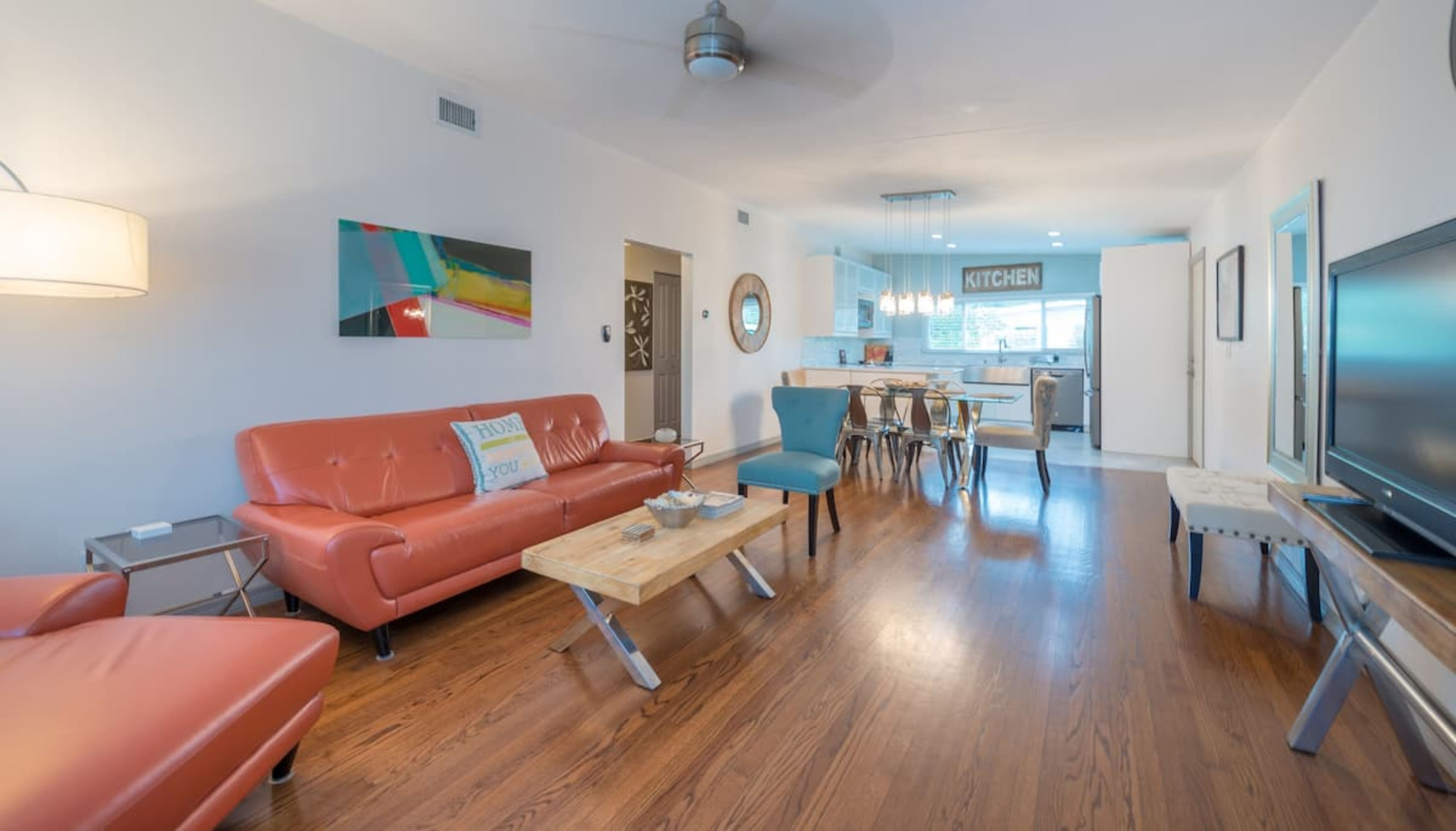 A modern living room with an orange sofa, wooden tables, and an open kitchen in the background.