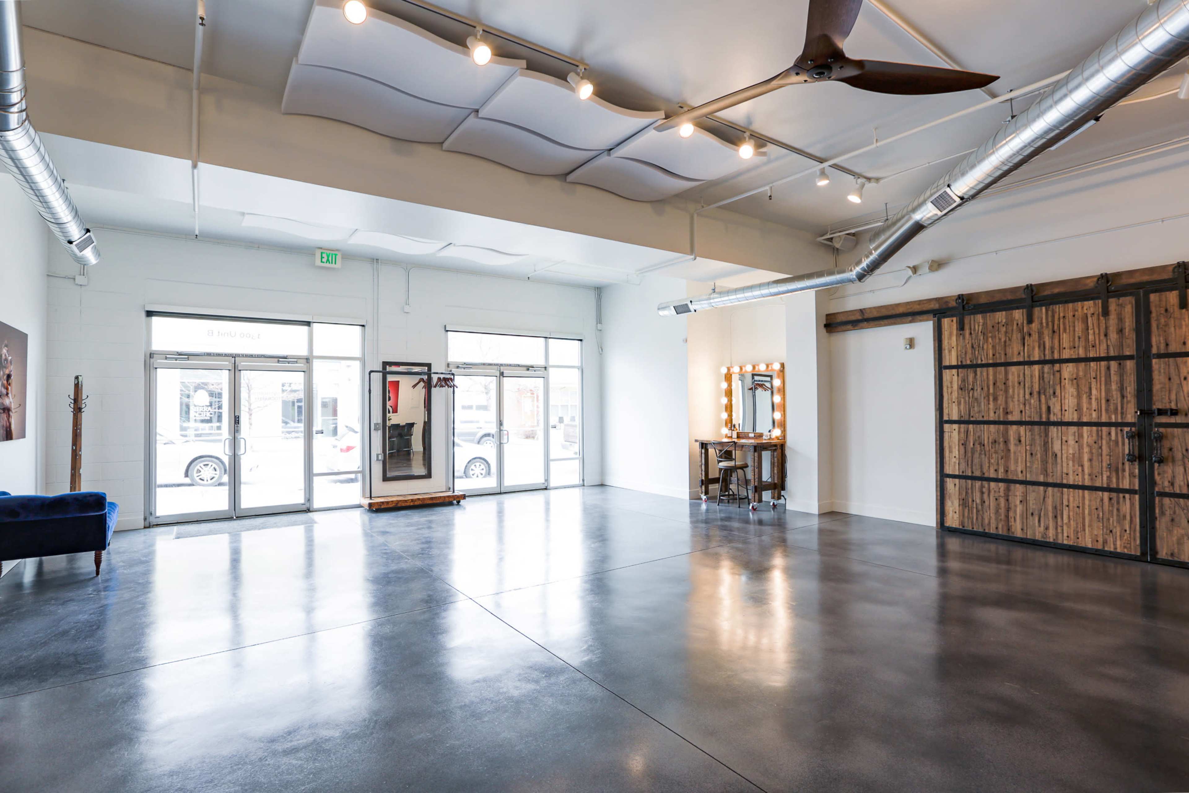 A spacious, well-lit interior with polished concrete floors, large windows, and a vanity mirror setup against a wooden wall.