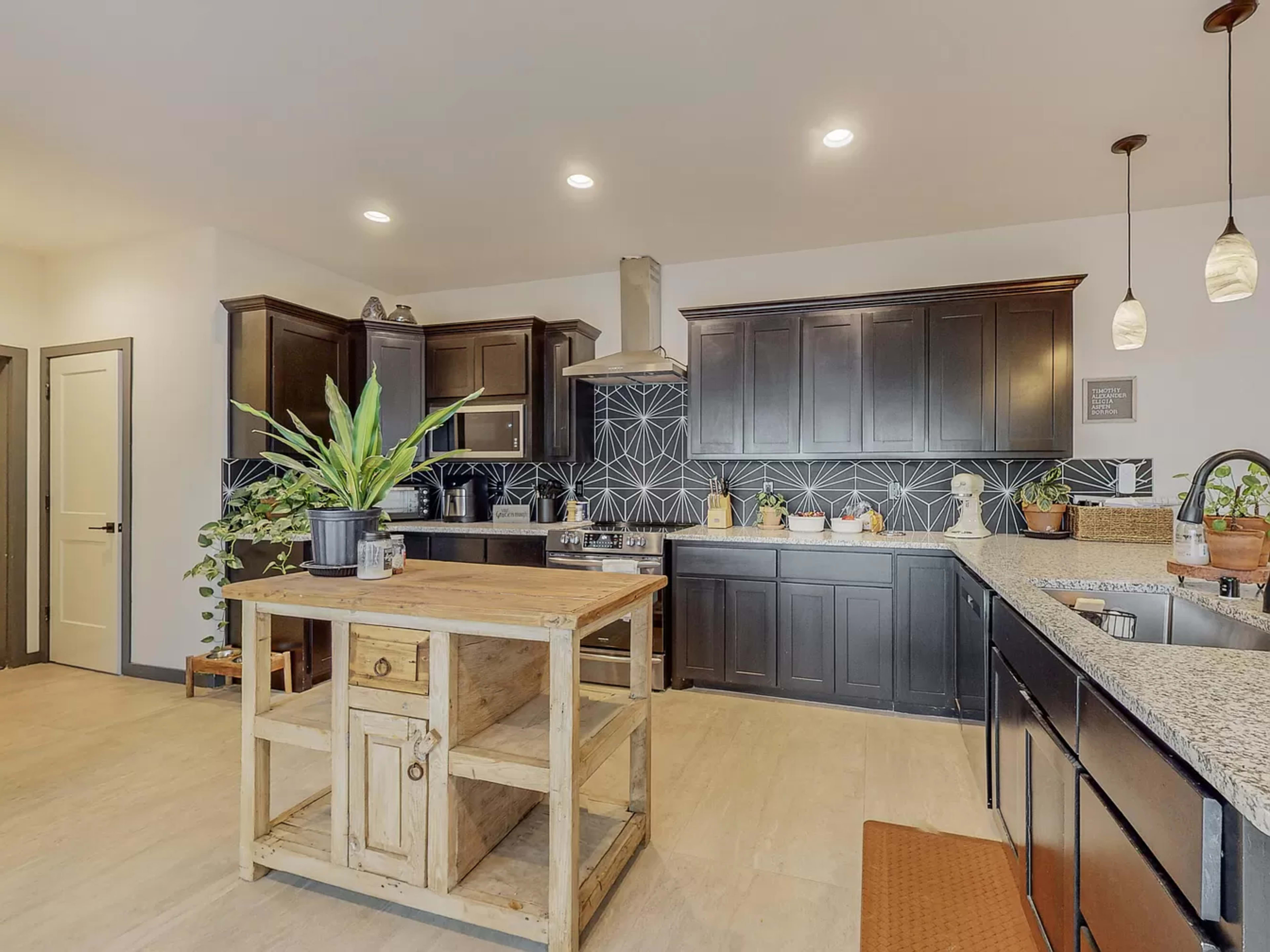 The kitchen features dark cabinetry, a central wooden island, and a geometric backsplash.