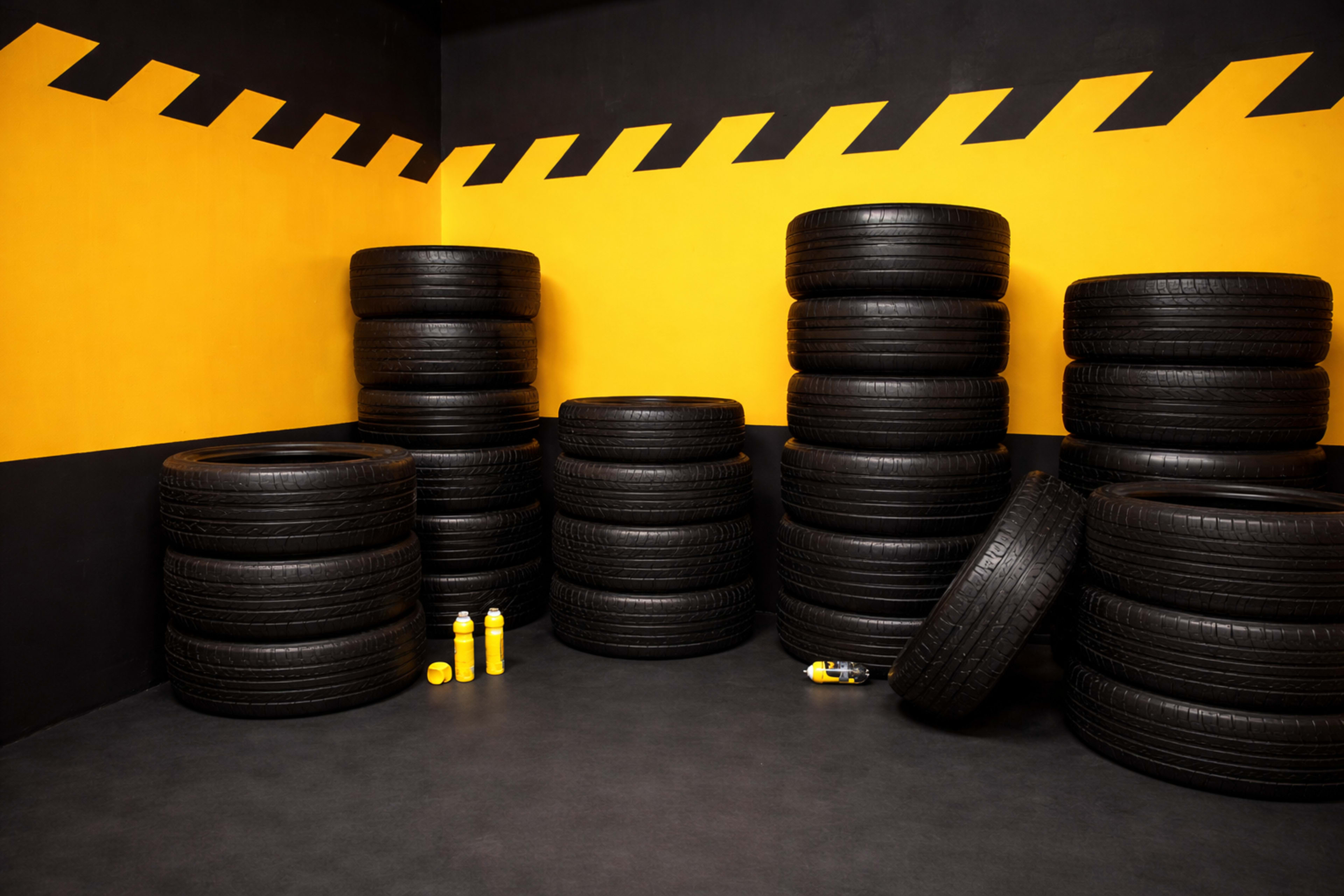 The image shows a corner of a room with multiple stacks of black tires against a backdrop of a black and yellow wall.