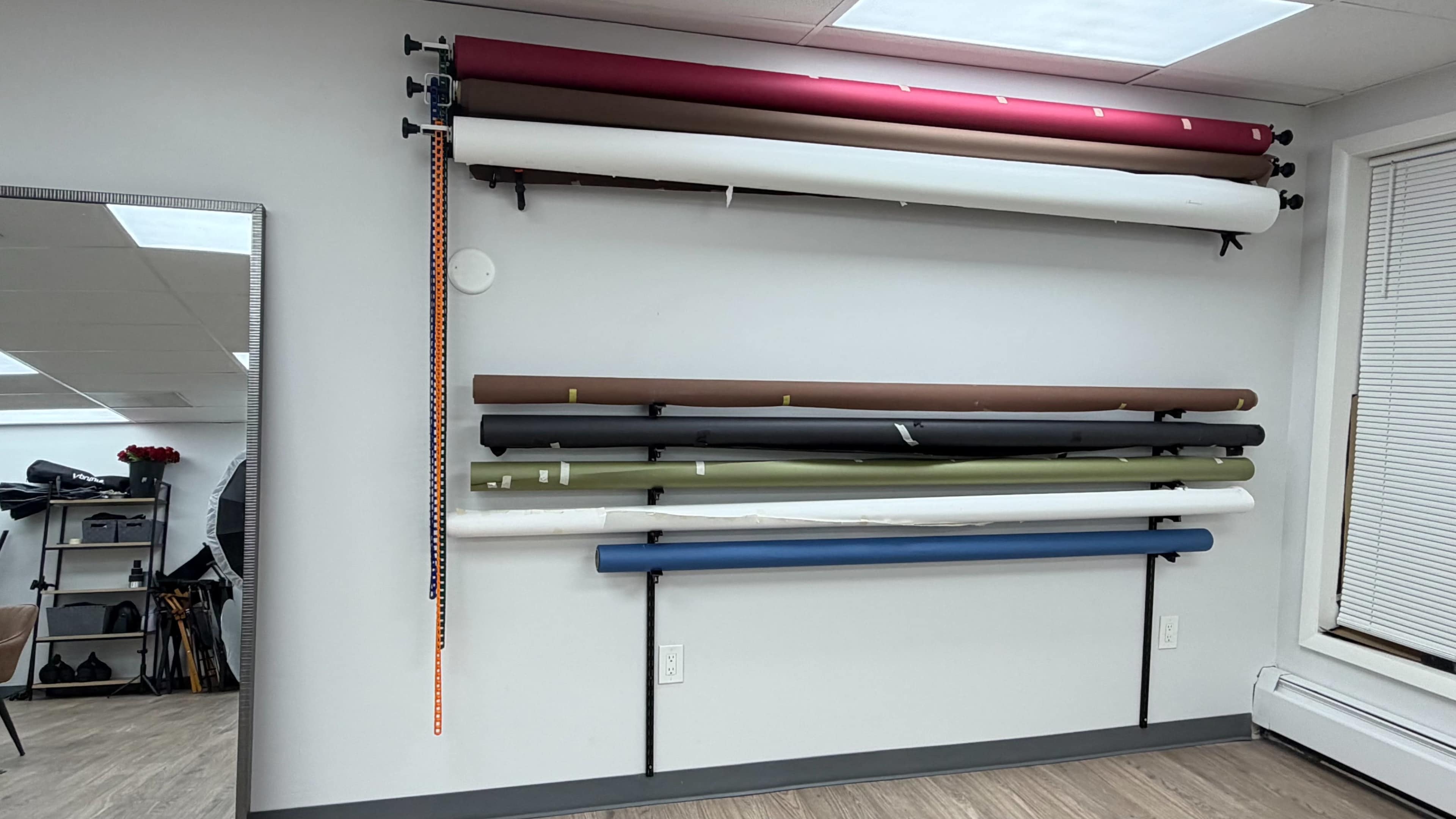 The image shows a wall-mounted display of rolled paper backdrops in various colors, organized horizontally on a rack.