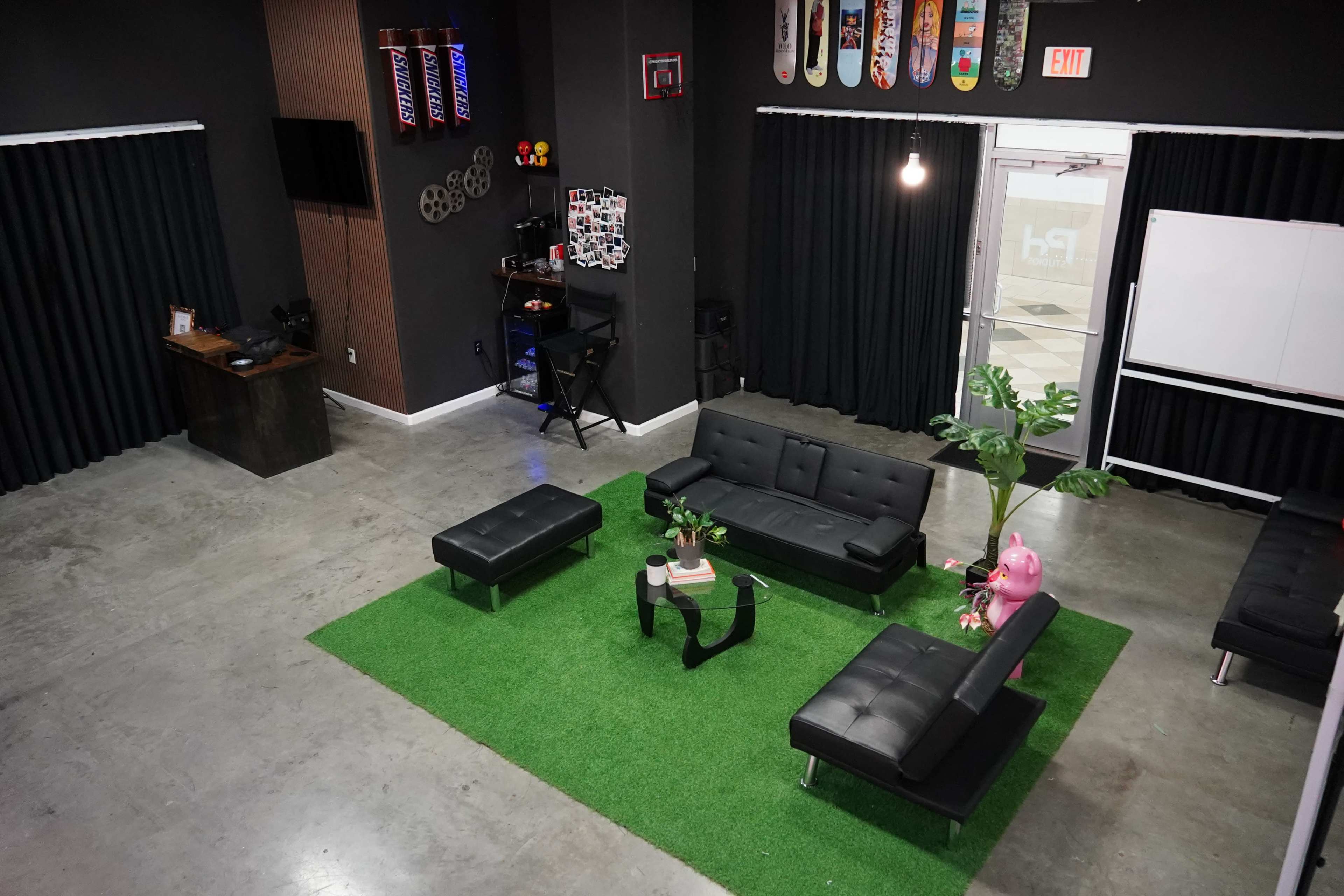 The image shows a modern lounge area with black furniture, a green carpet, and a wall adorned with skateboard decks and a TV.