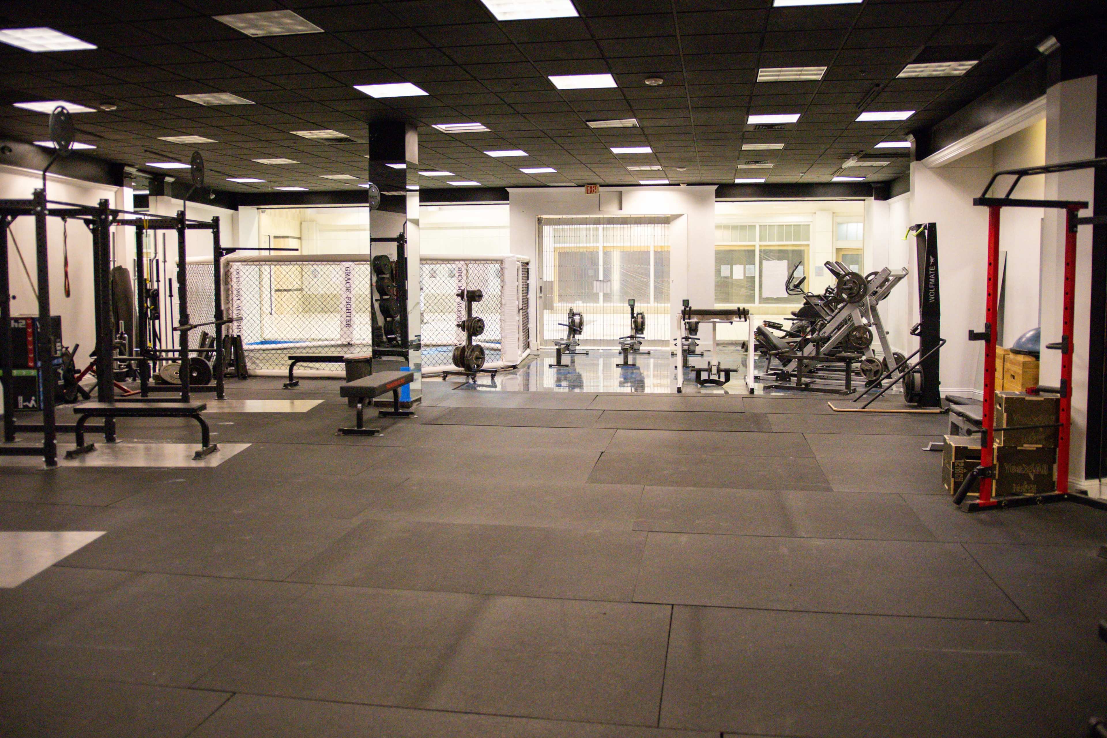 A spacious gym interior with various exercise equipment, including weightlifting stations and cardio machines, under ceiling lights.