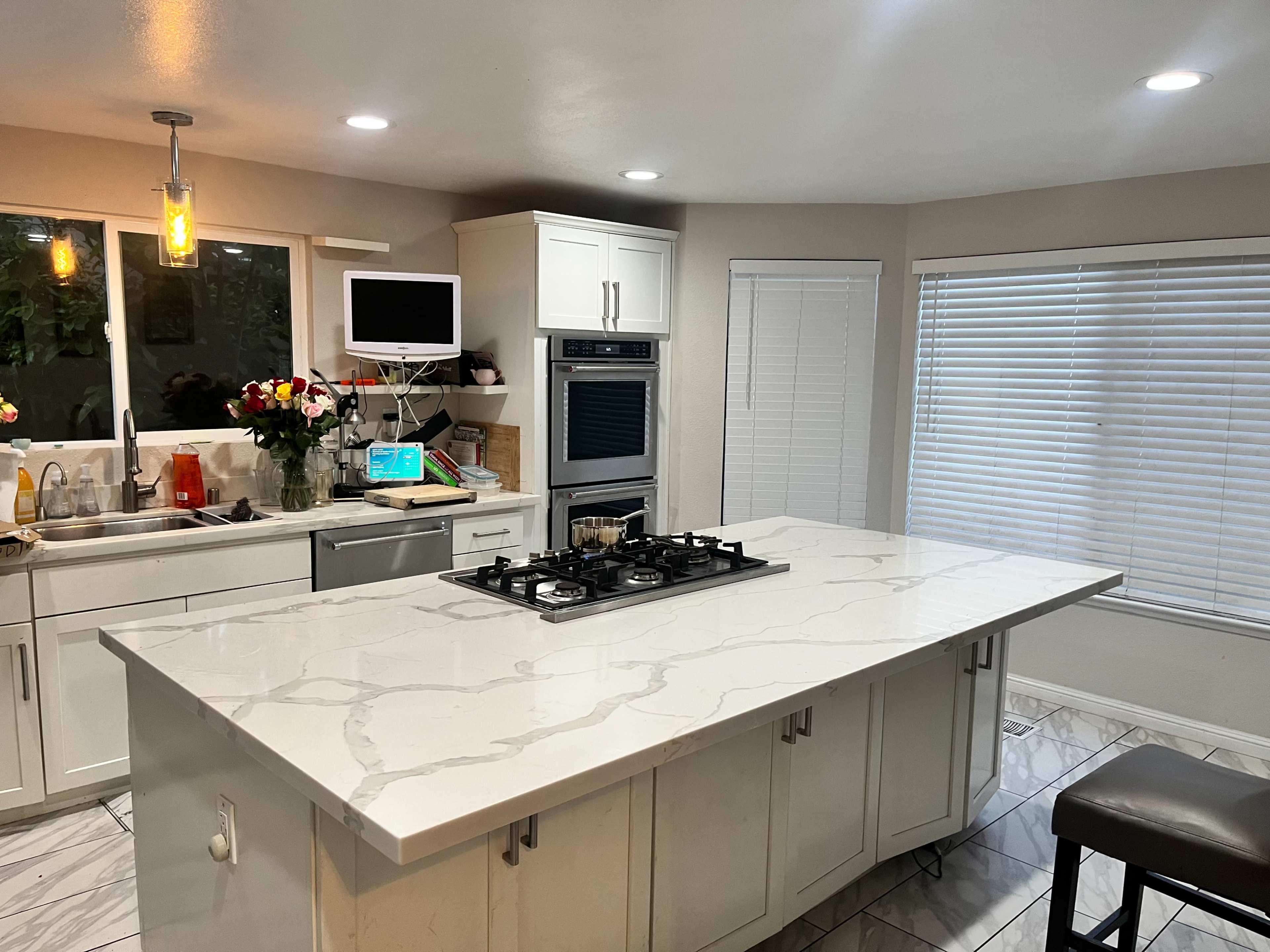A modern kitchen with a central island featuring a gas cooktop, white cabinetry, and a window above the sink.