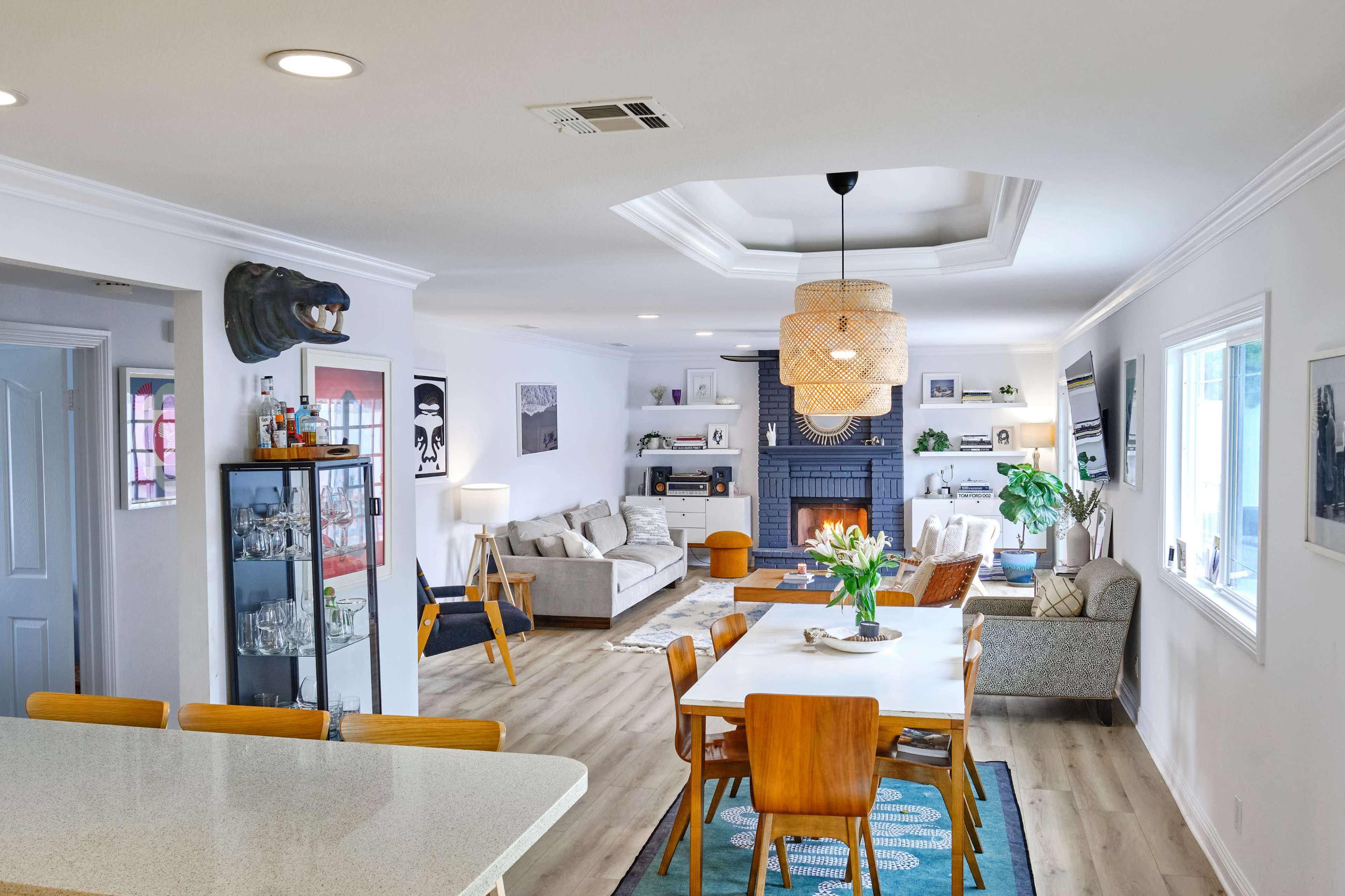 A spacious living area features a dining table, a cozy seating arrangement, and a fireplace, accented by modern decor and natural light.