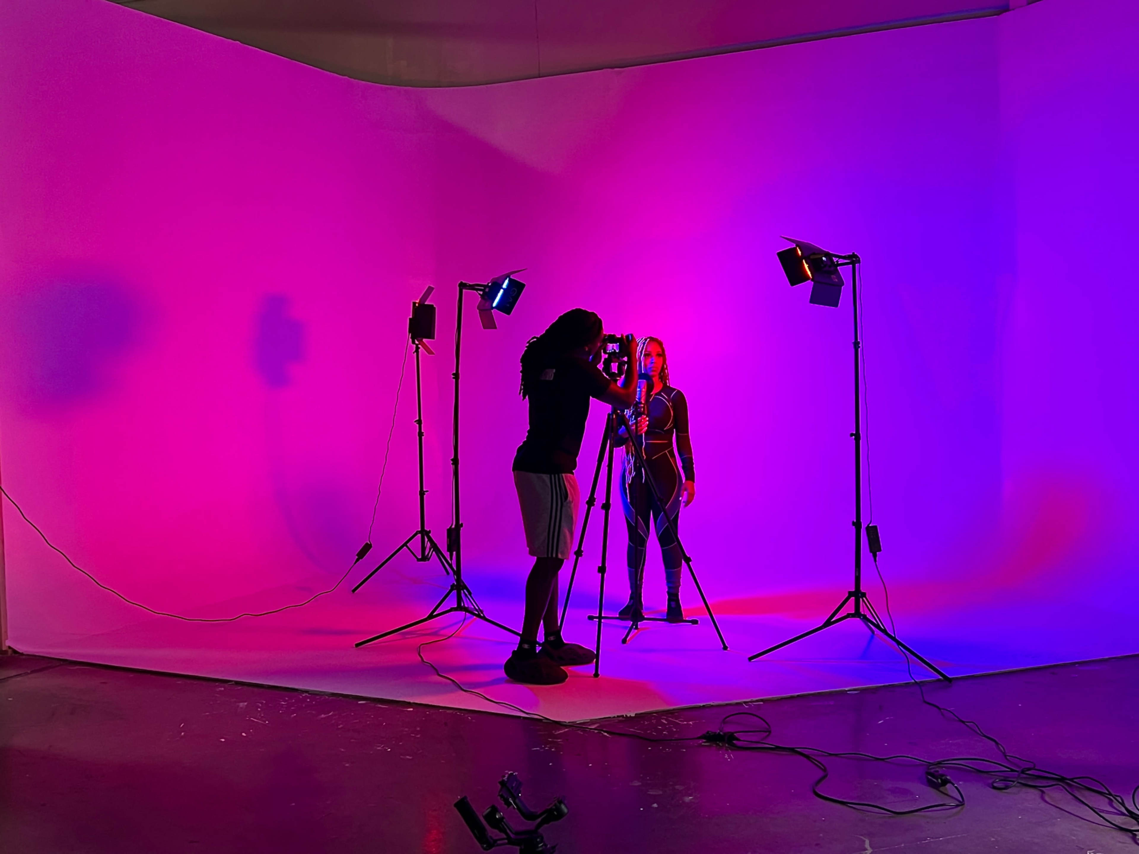 A photographer captures an image of a model in a brightly lit studio with pink and blue backgrounds.