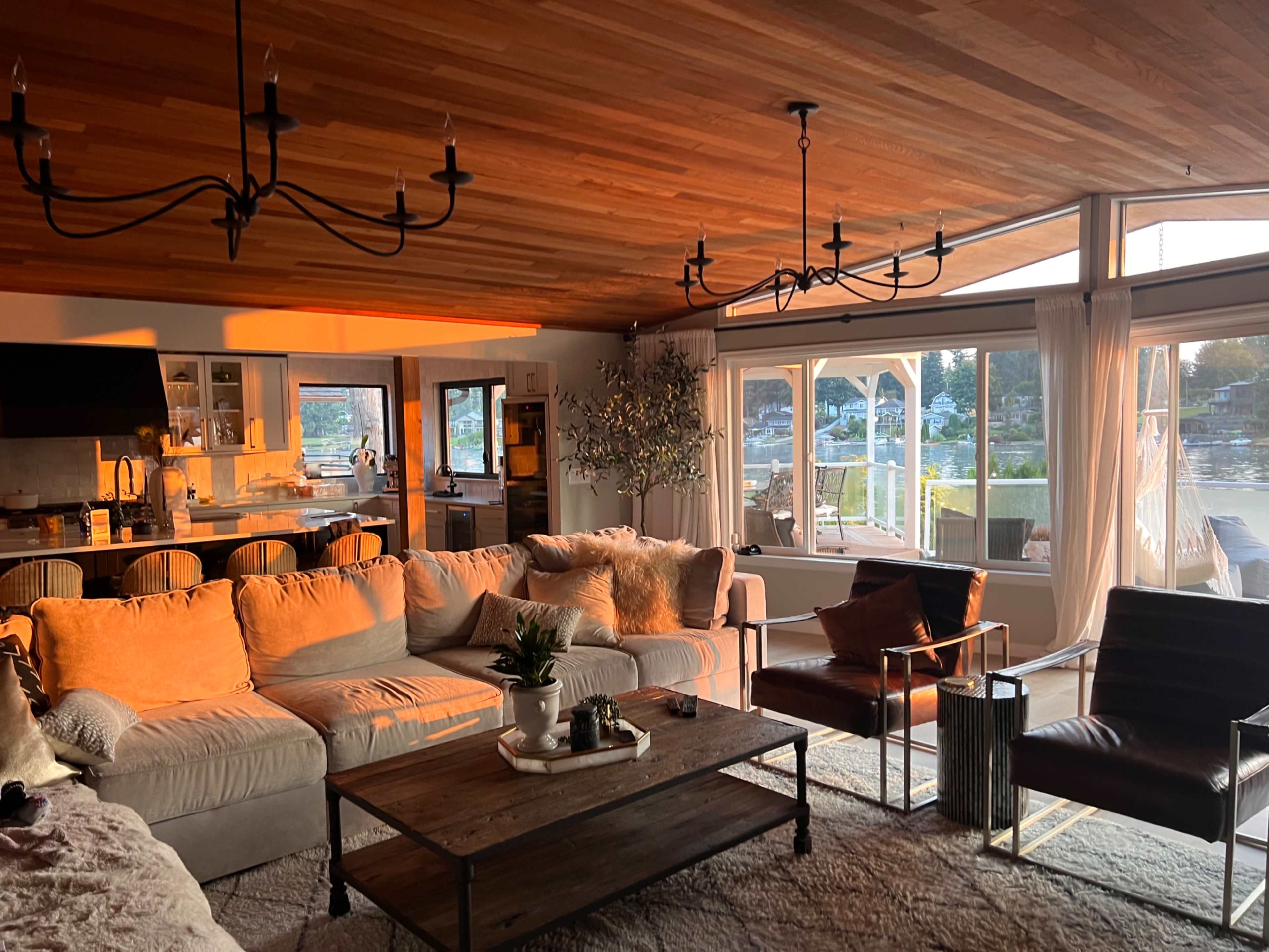 A cozy living room with a beige sectional sofa, a wooden coffee table, and large windows overlooking a waterfront view.