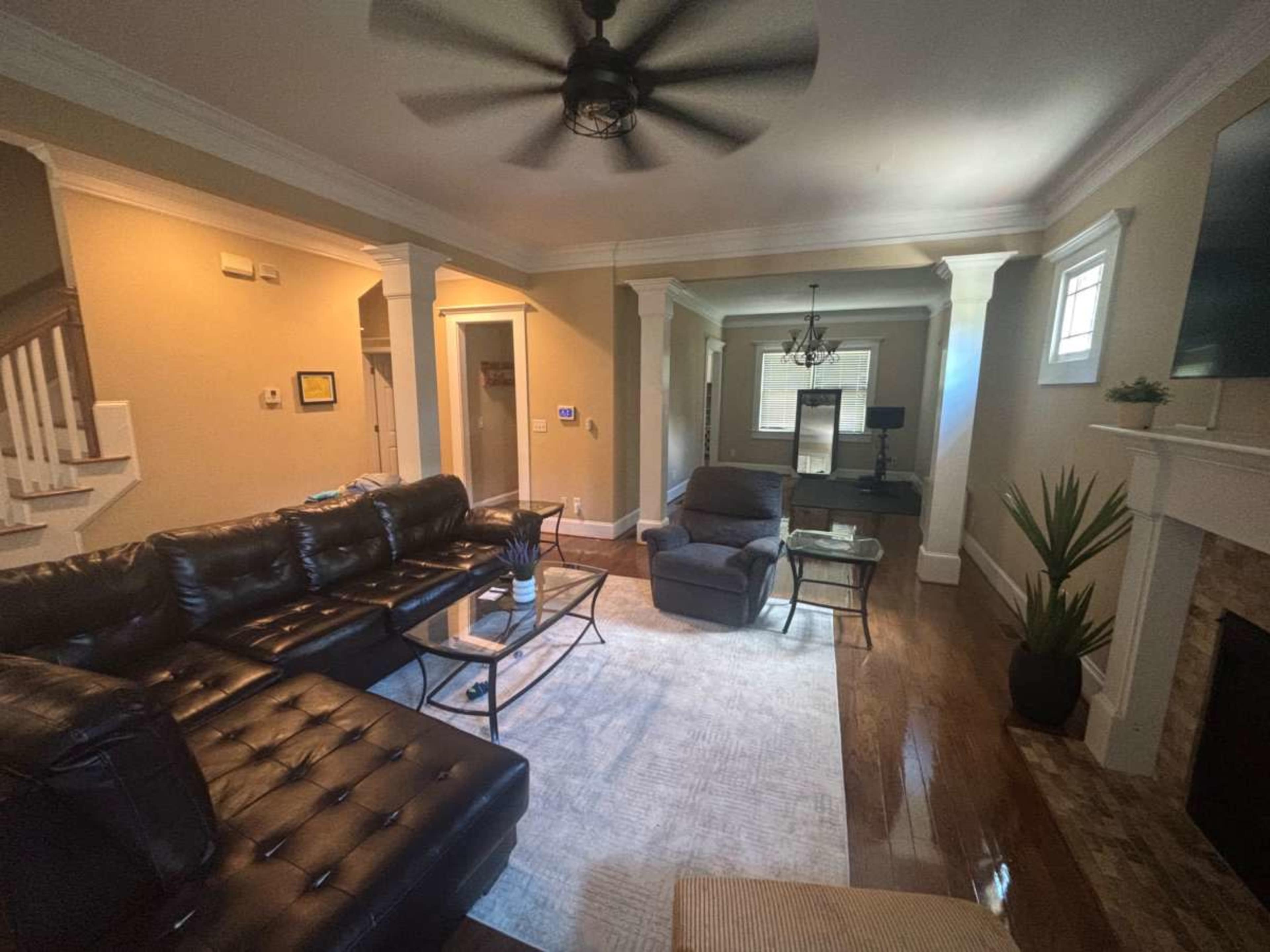 The image shows a well-furnished living room with a black sectional sofa, a recliner, and a coffee table on a light-colored rug.