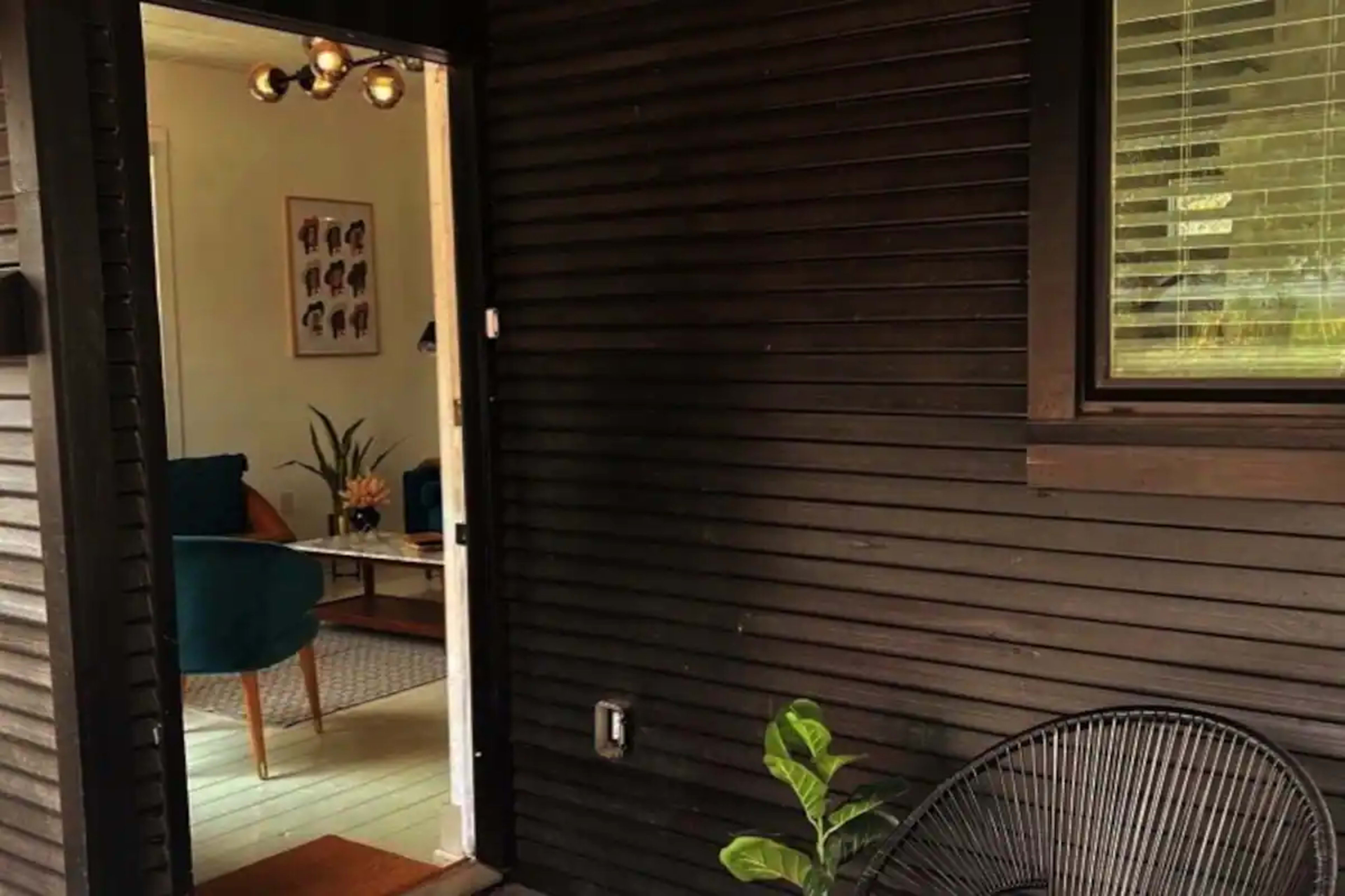 A partially open black door reveals a glimpse of a living room with teal chairs and a wall adorned with framed artwork.