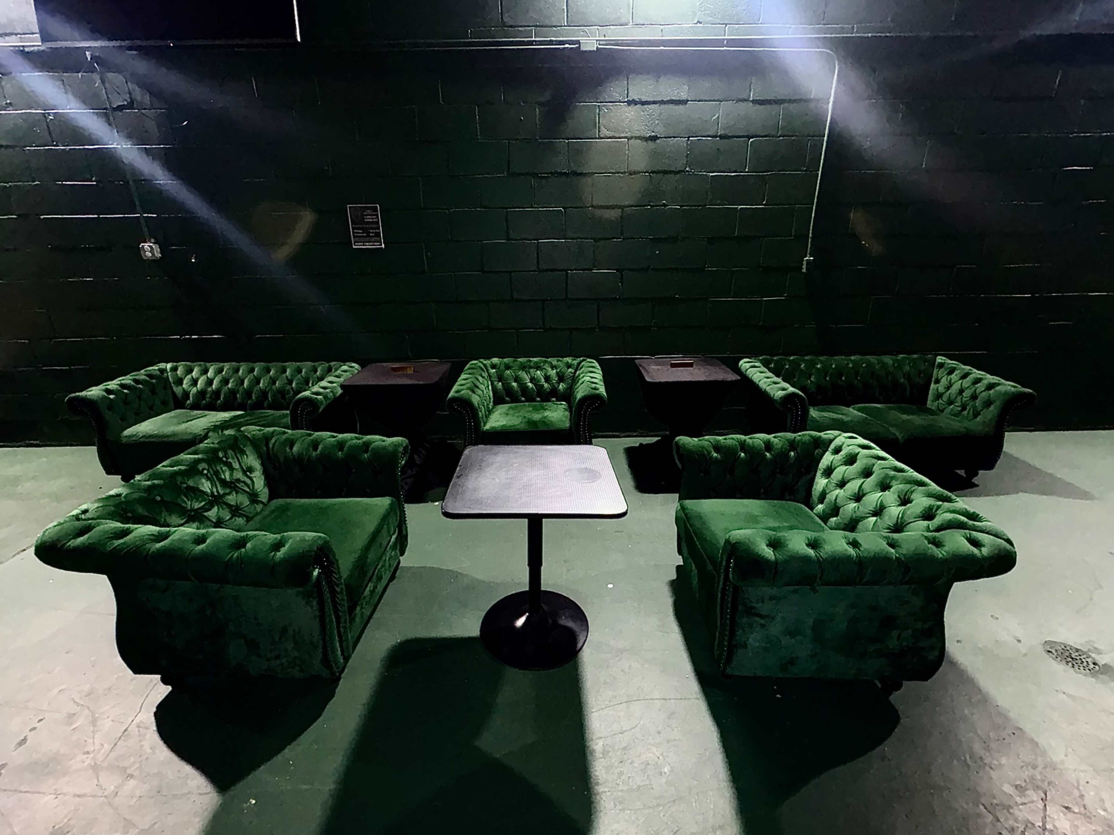 The image shows several green tufted armchairs arranged around a small black table in a dimly lit room.