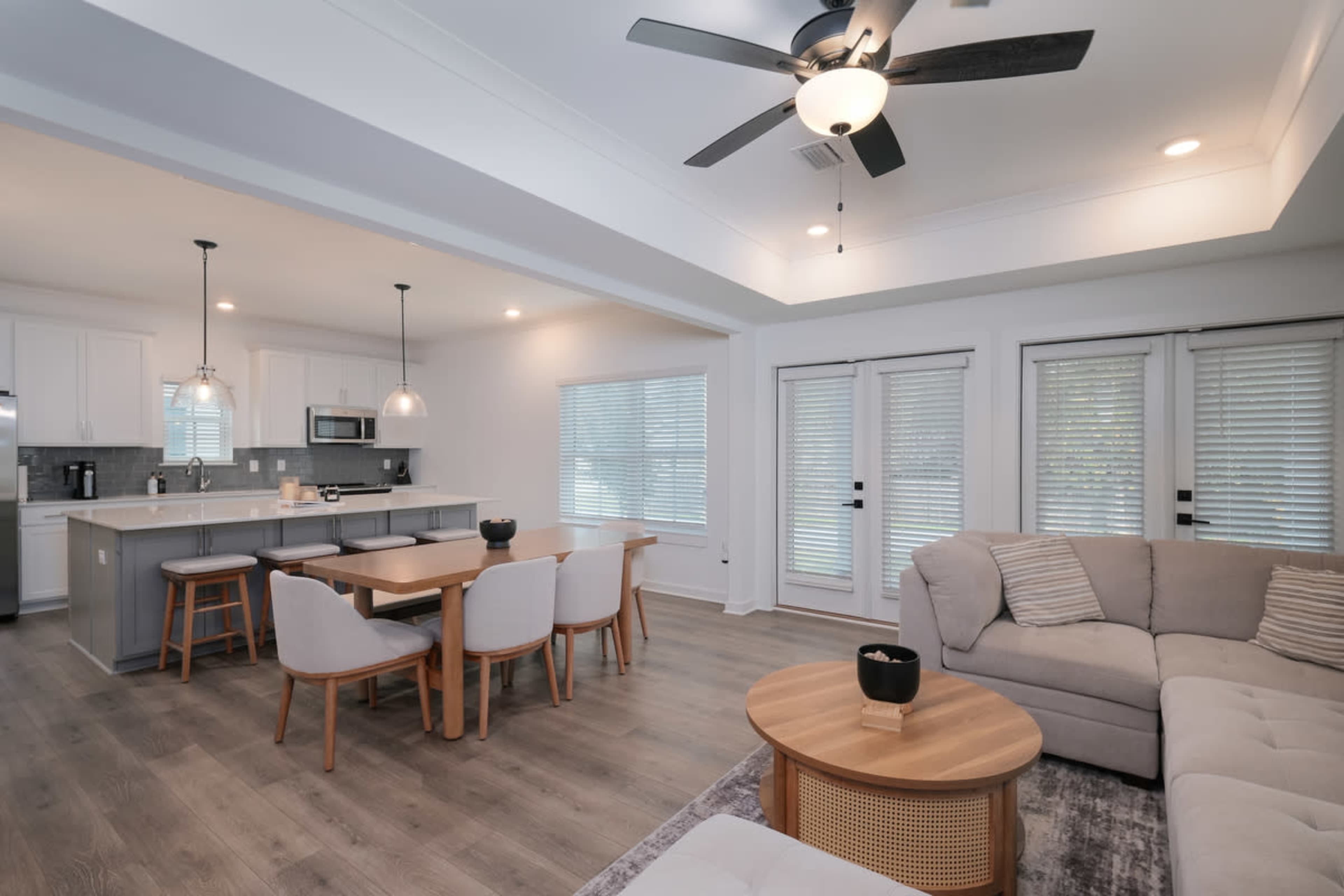 The image shows a modern open-concept living area that includes a kitchen with an island, a dining table, and a comfortable seating area.