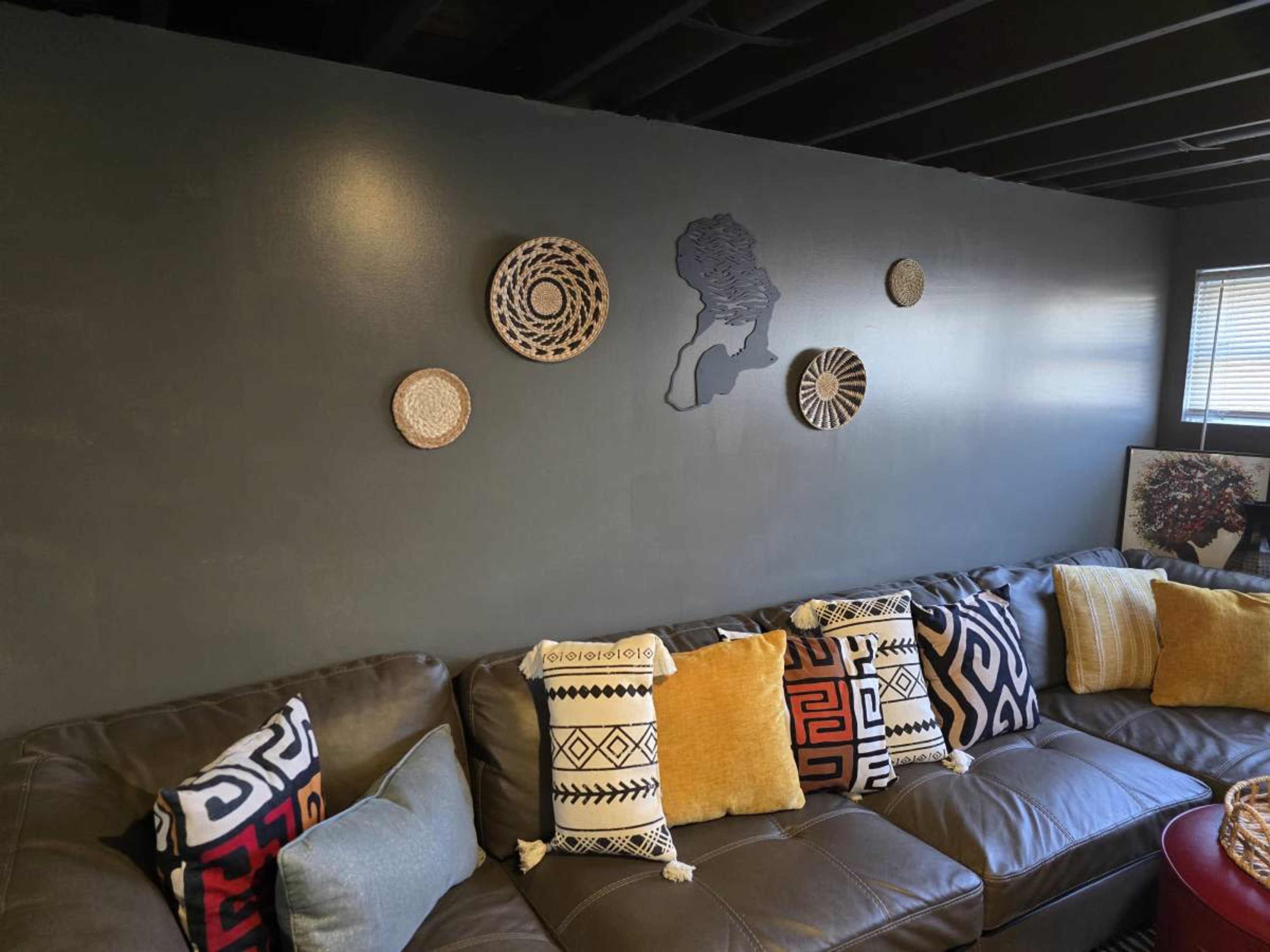 A sectional leather sofa is adorned with patterned pillows and positioned against a dark gray wall featuring decorative woven plates and a wall art silhouette.